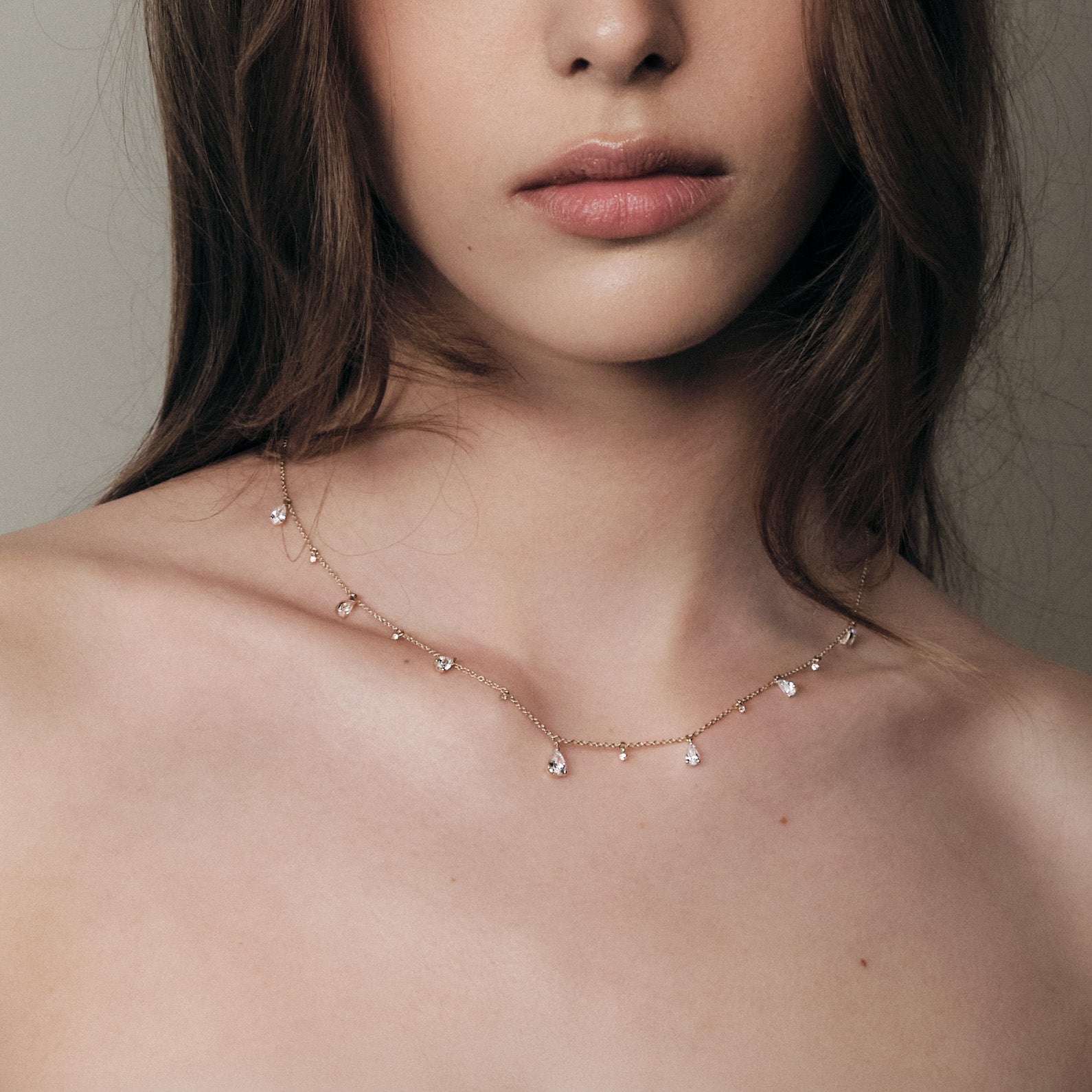 Close-up of a woman wearing a delicate teardrop diamonds necklace with a neutral background.