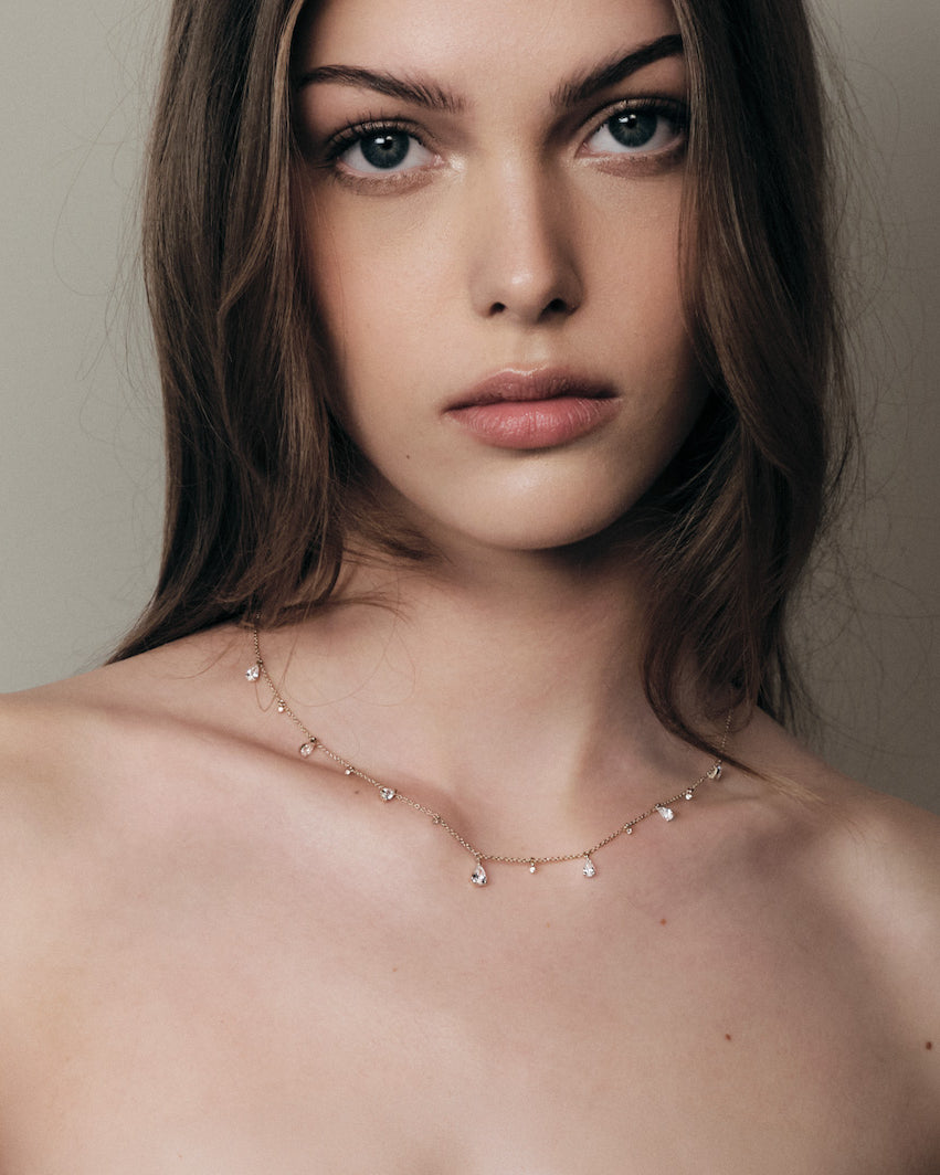 Woman wearing a delicate teardrop diamonds necklace against a neutral background.