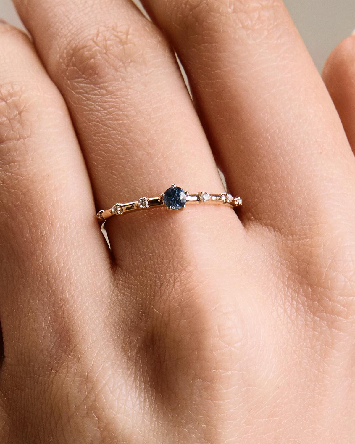 A gold band ring featuring a central sapphire with smaller diamond accents around it, presented on an a hand.