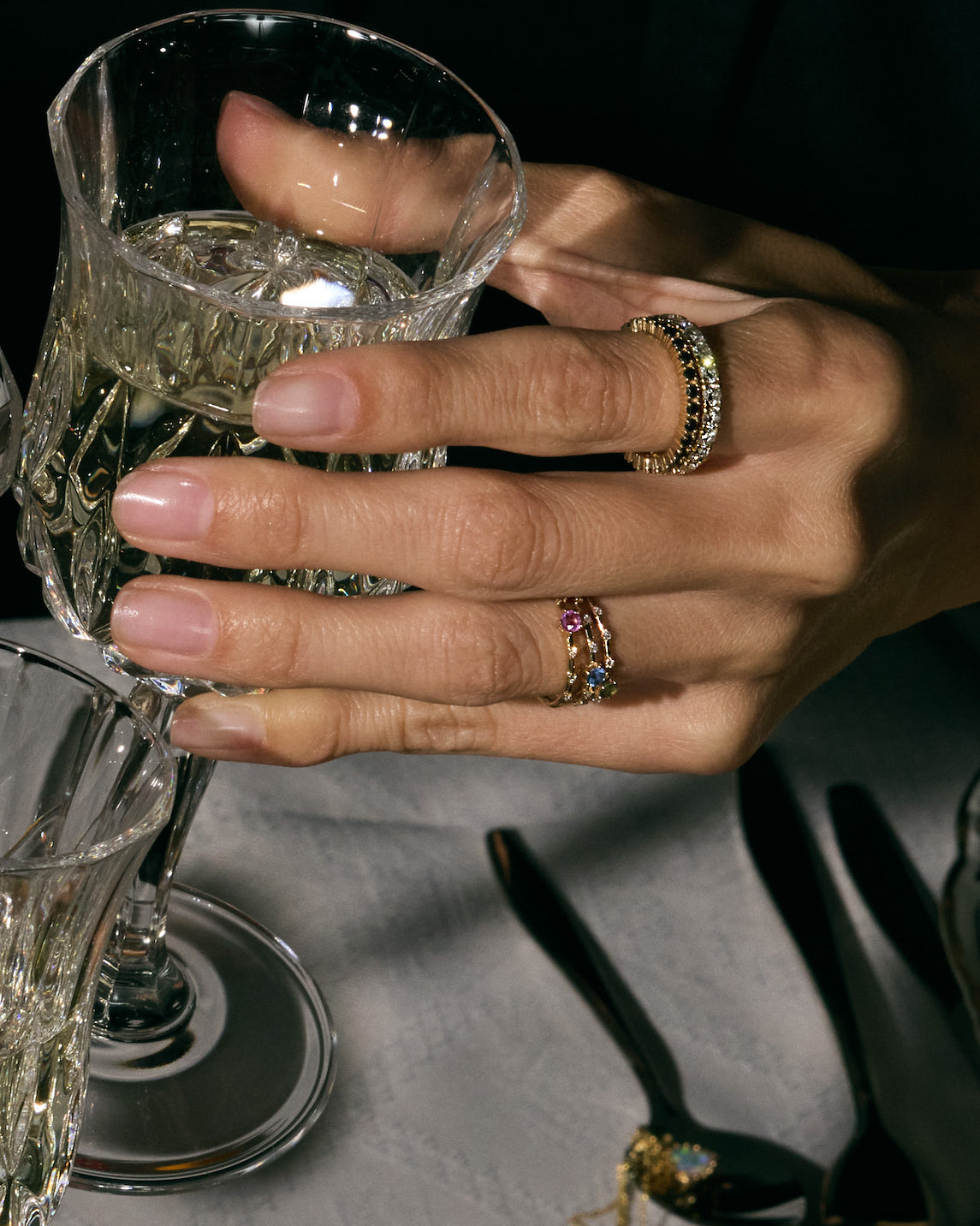 Hand full of rings, eternity black and white diamond rings, holding a crystal glass with another glass in the foreground, on a dark background