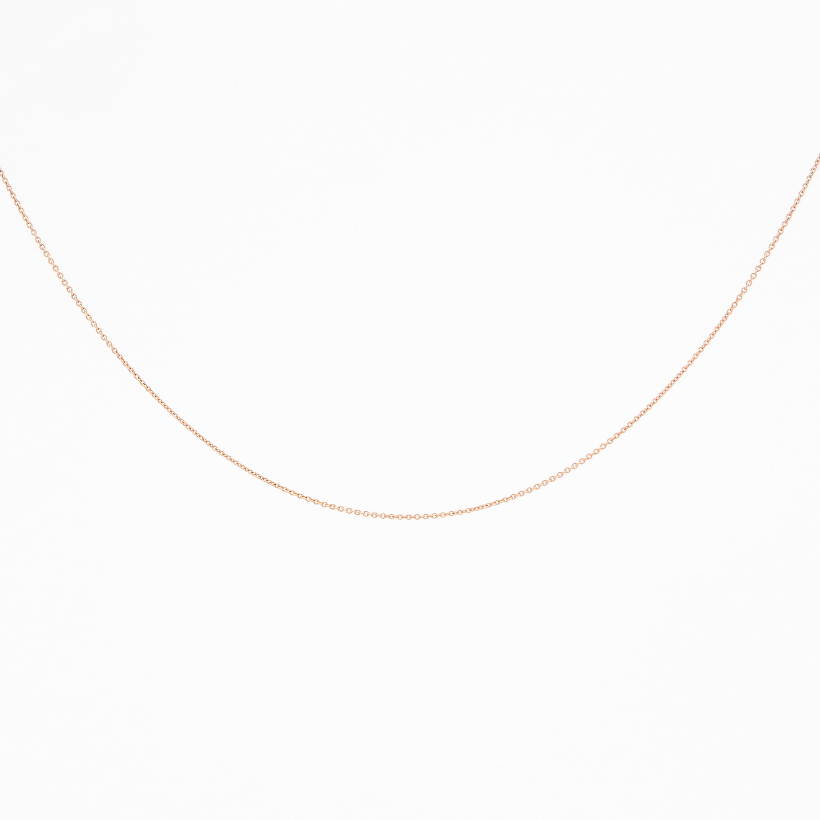 A rose gold chain necklace laid out on a plain surface.