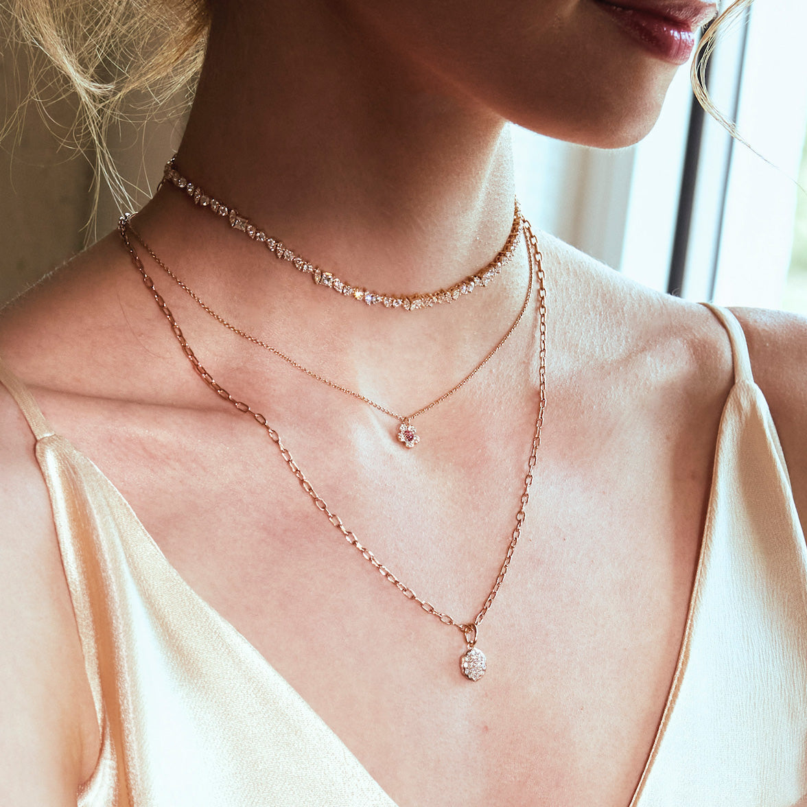 Close-up of a person wearing multiple rose gold necklaces with small pendants.