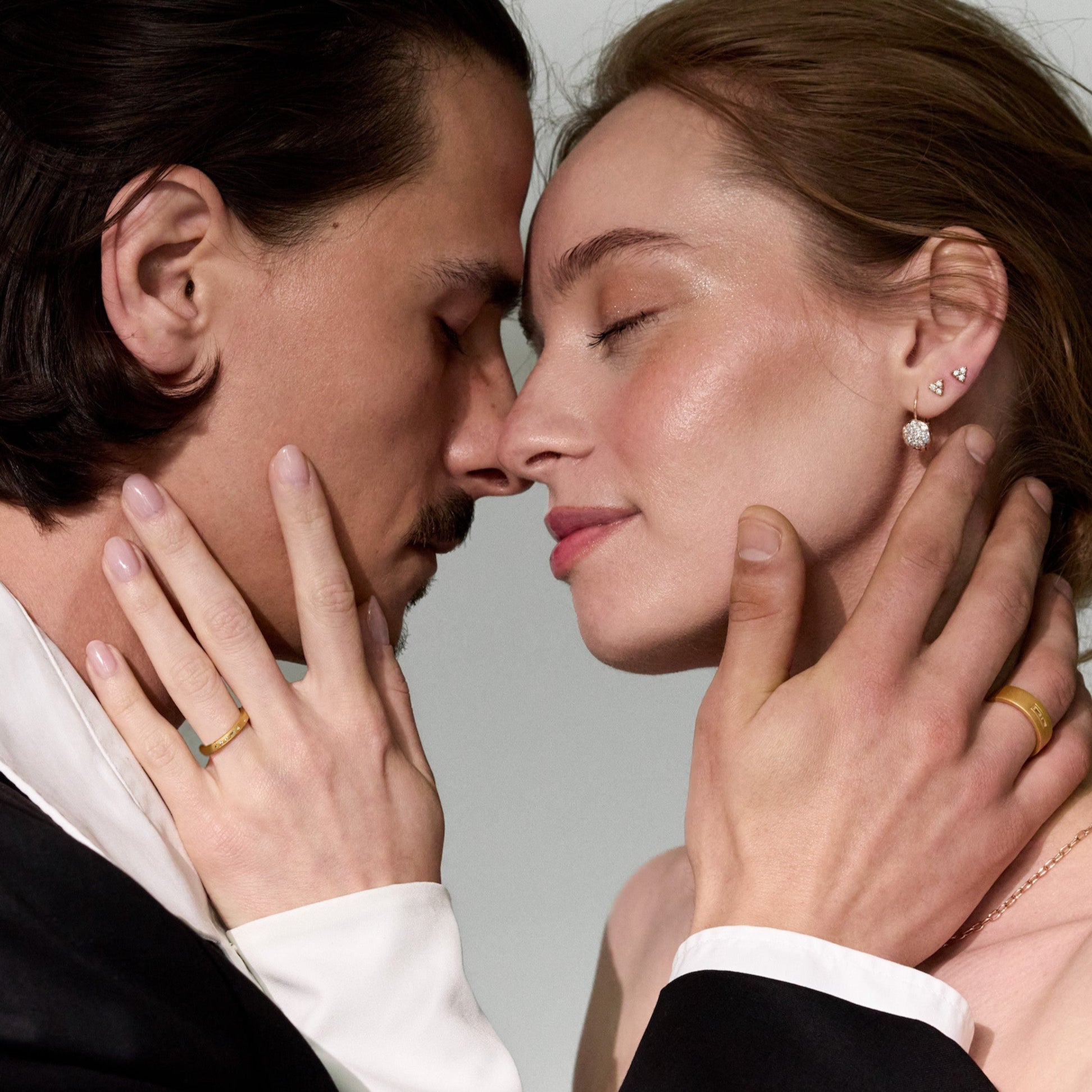 Close-up of a couple having an intimate moment, with a focus on gold and diamonds jewelry, including earrings and wedding band rings with morse code diamonds.