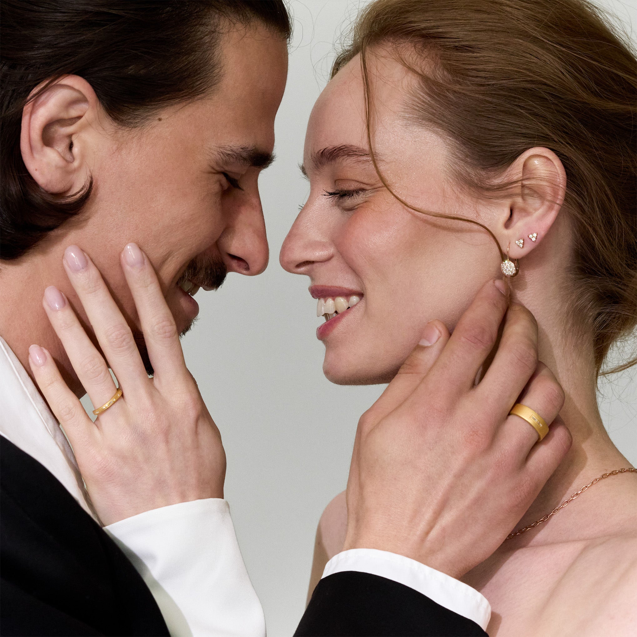 Close-up of a couple having an intimate moment, with a focus on gold and diamonds jewelry, including earrings and wedding band rings with morse code diamonds.