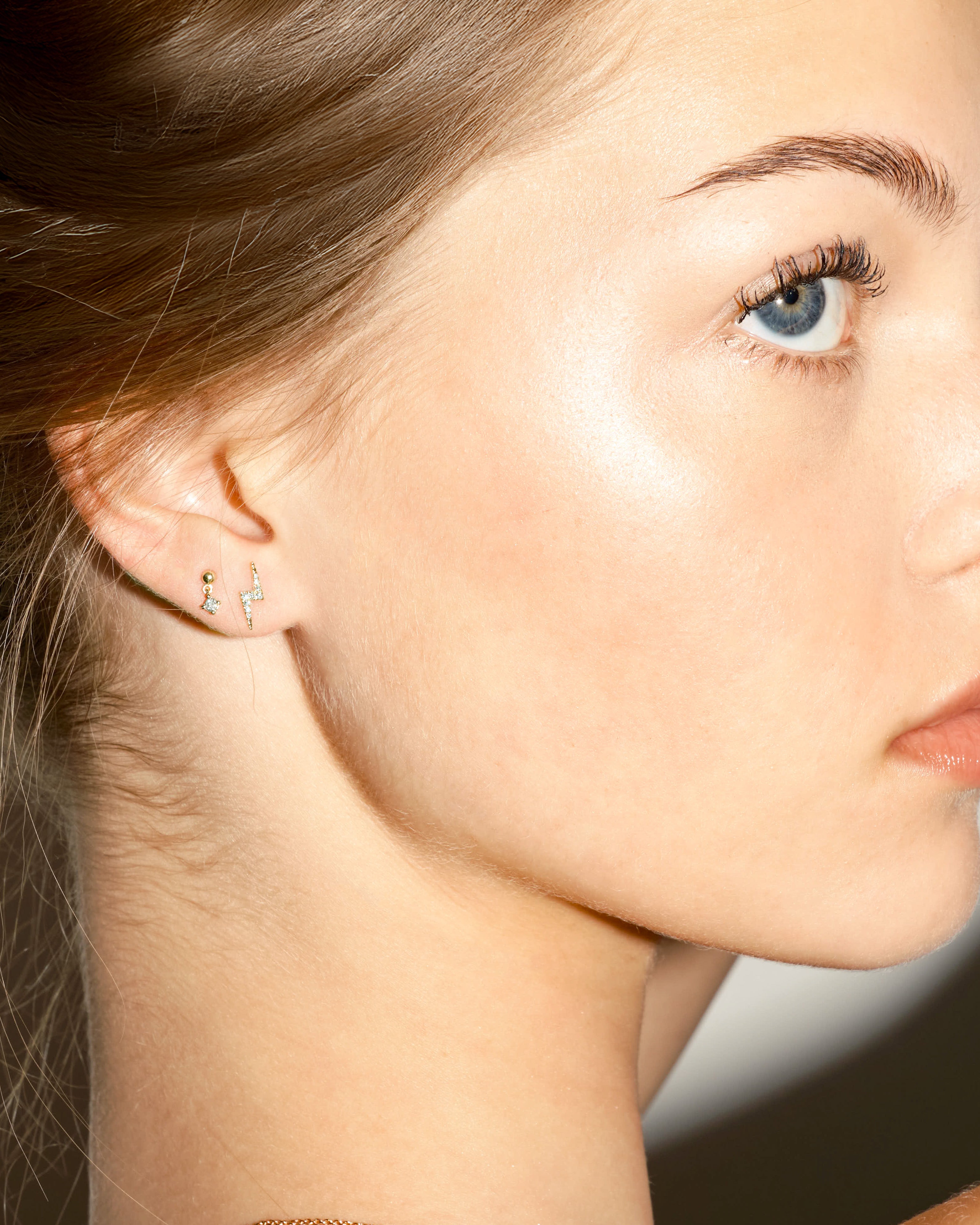 Close-up of a woman's profile with a focus on her earrings, a flash shape earring and a floating dot diamond earring.