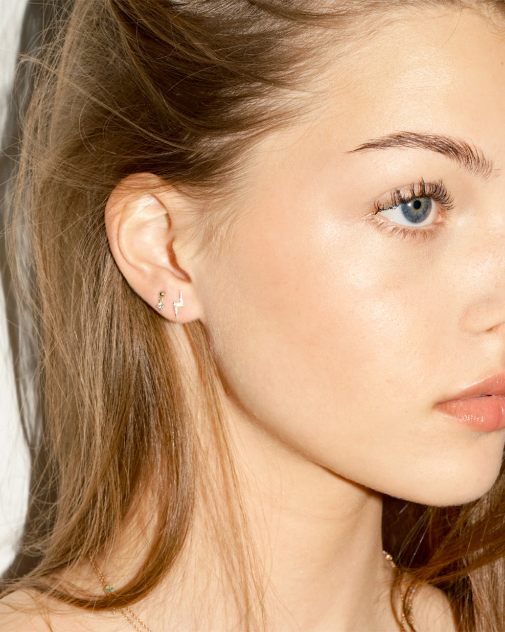 Close-up of a woman wearing small earrings, a floating diamond dot, and a a flash diamonds stud, with a plain background