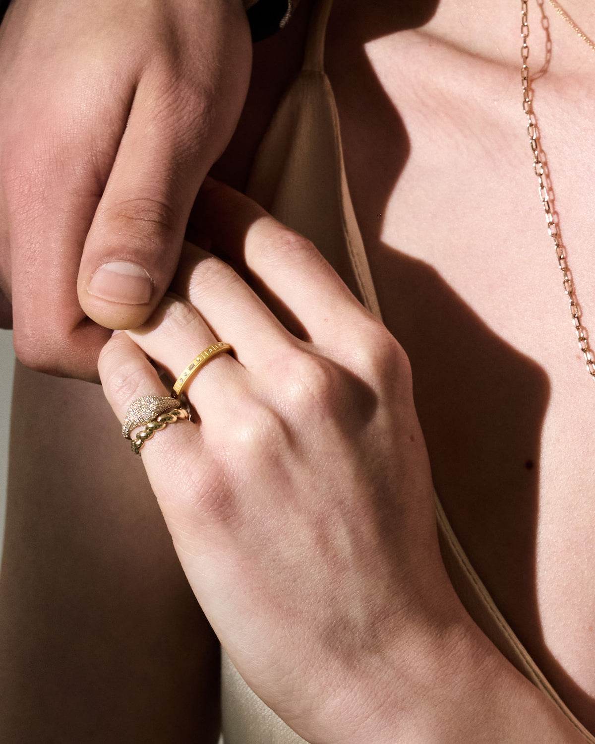 Close-up of holding hands with gold rings and a necklace against a neutral background