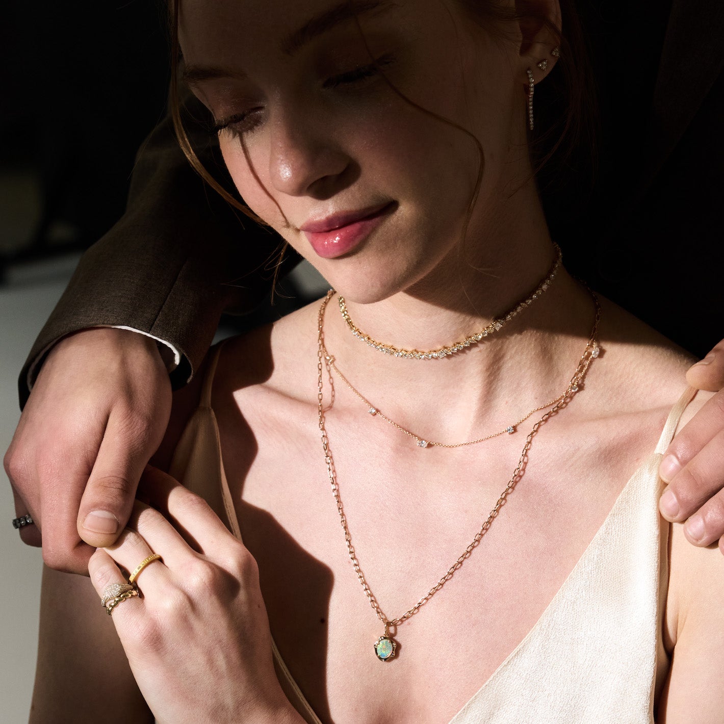 Woman wearing multiple diamond necklaces and diamond rings with a dark background