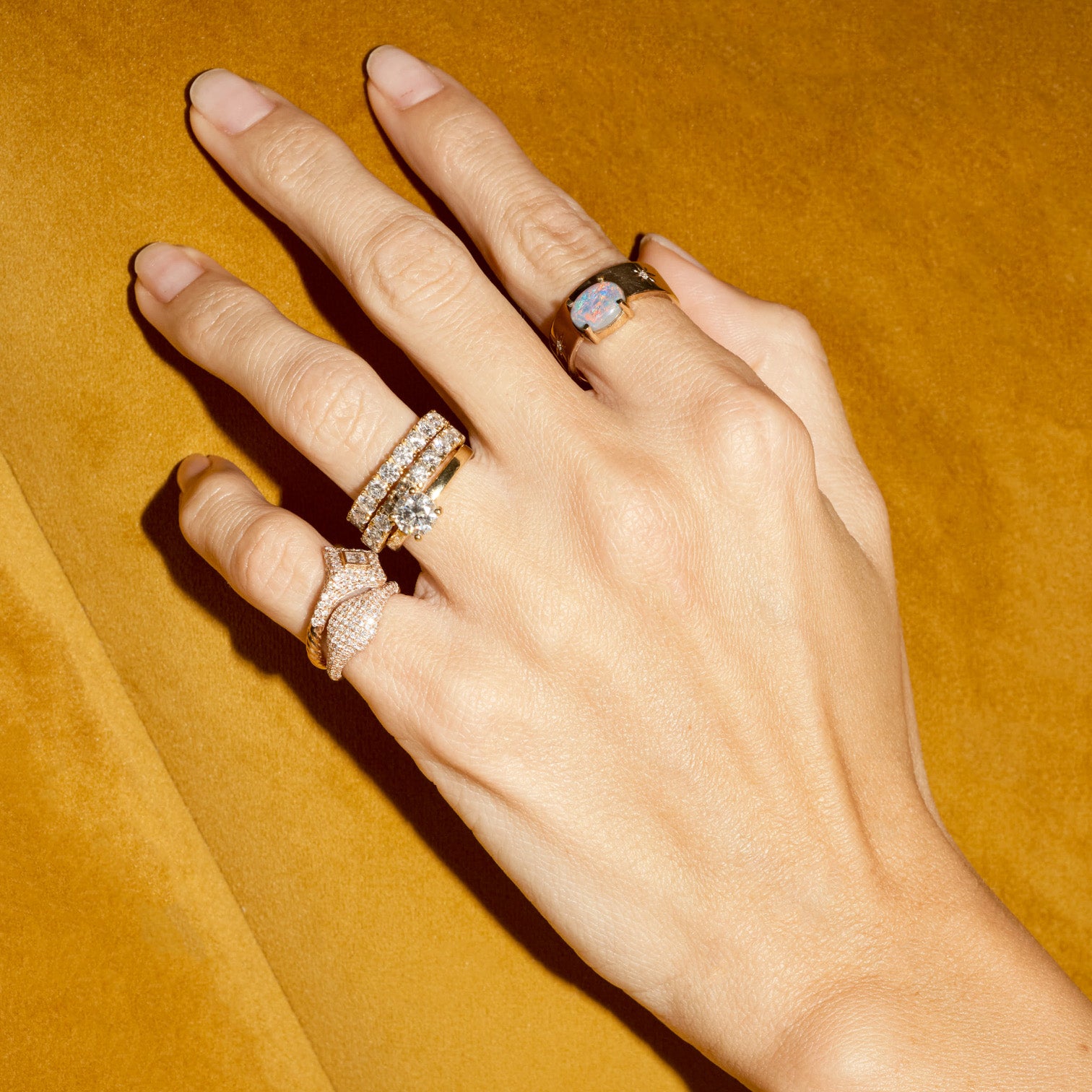 Hand wearing multiple rings on a mustard yellow background