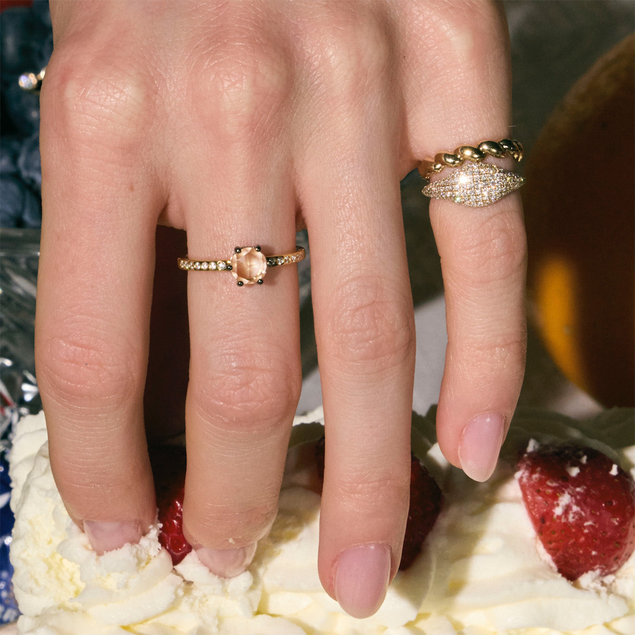 Hand picking up a piece of cake, wearing two diamond rings and a twisted pinky band