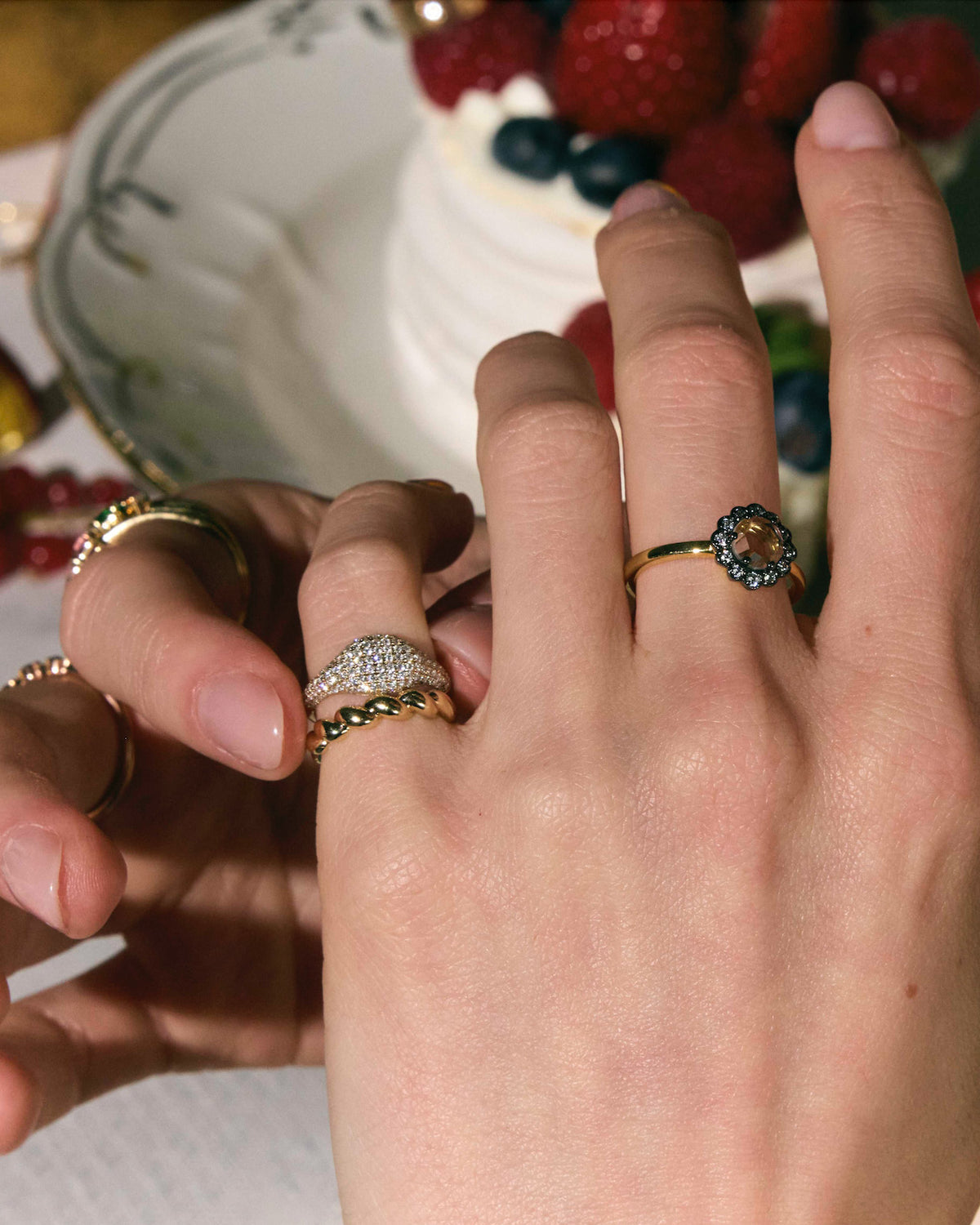 Close-up of hands wearing the most elegant diamond rings in front of a cake with berries