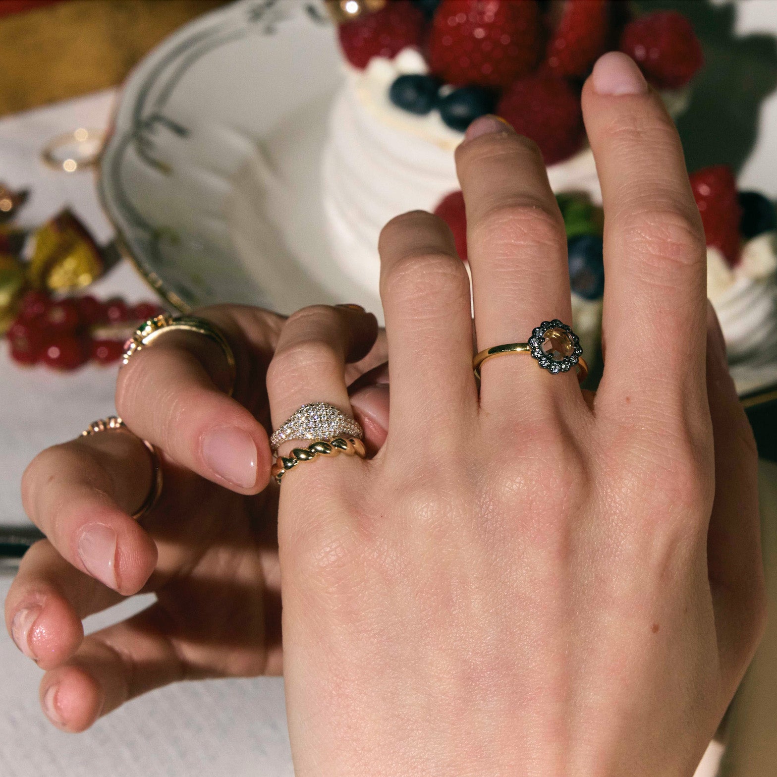 Close-up of hands wearing the most elegant diamond rings in front of a cake with berries