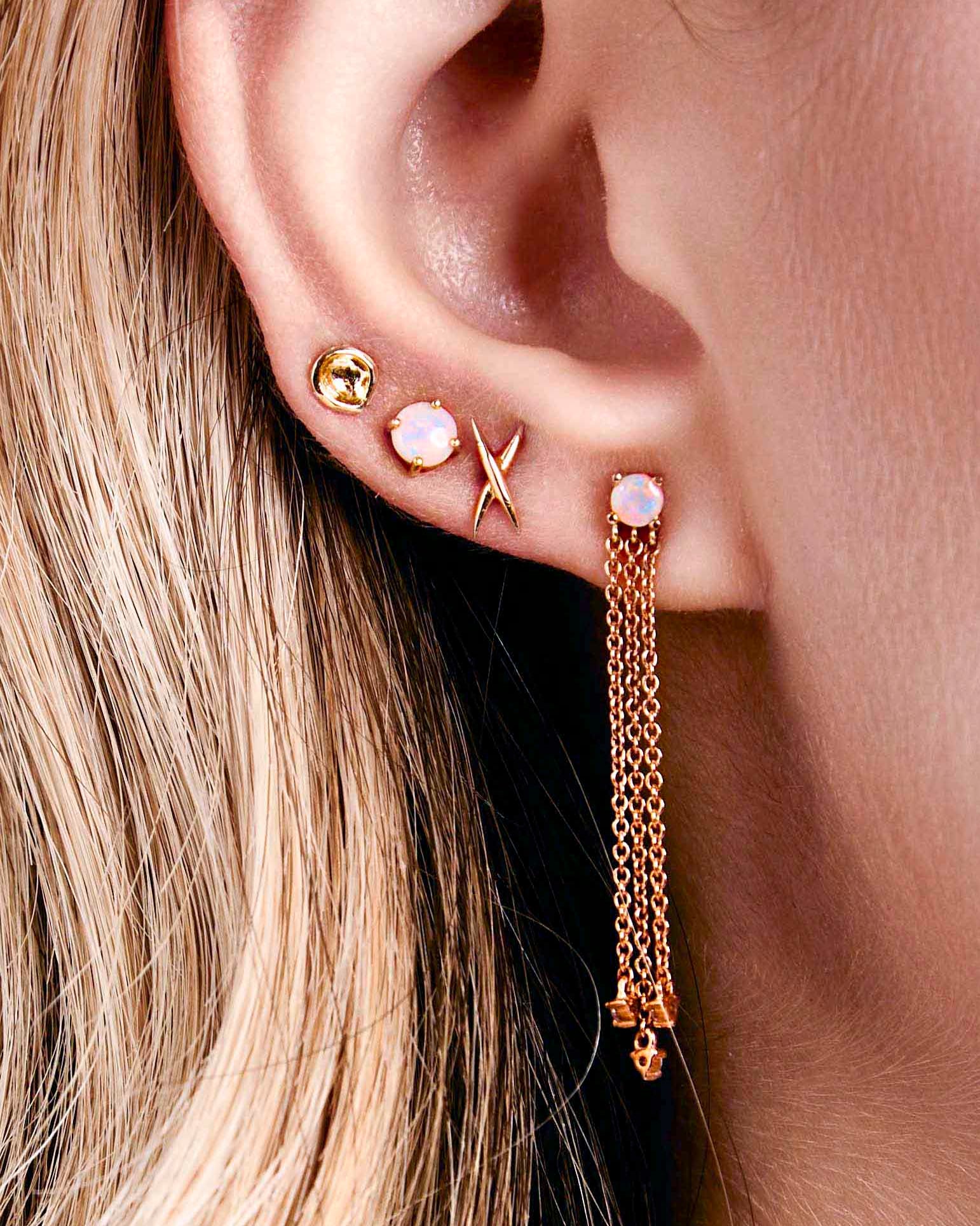 A pair of gold-colored stud earrings shaped like an X, australian opal studs on a ear.