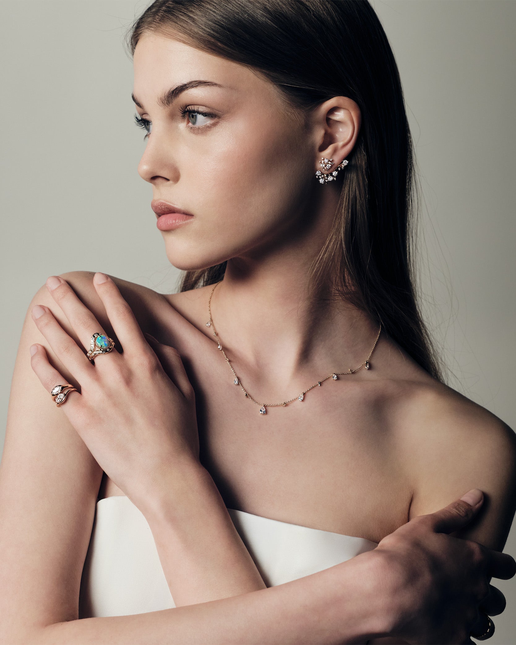 A woman wearing a ring with a australian opal and diamonds, two pinky ring with marquise diamonds set in curvy rose gold bands. She uis also wearing a teardrop diaomonds necklace and a cluster diamonds earcrawler earring.