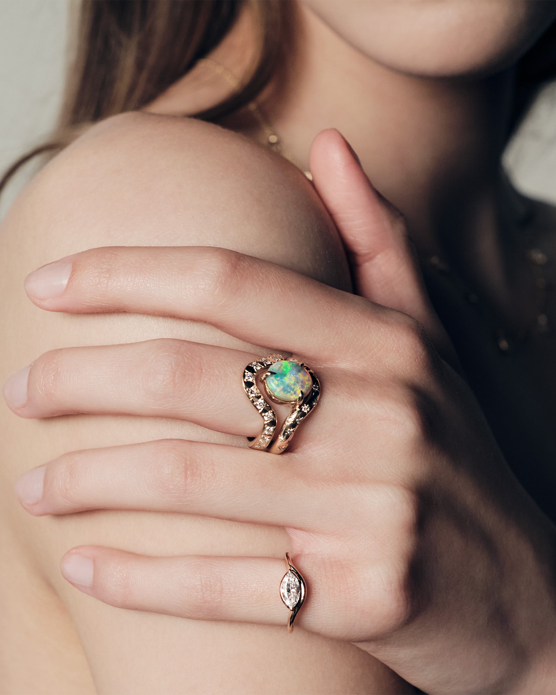 Close-up of a hand wearing a ring with a australian opal and diamonds, and a pinky ring with a marquise diamond set in a curvy band.