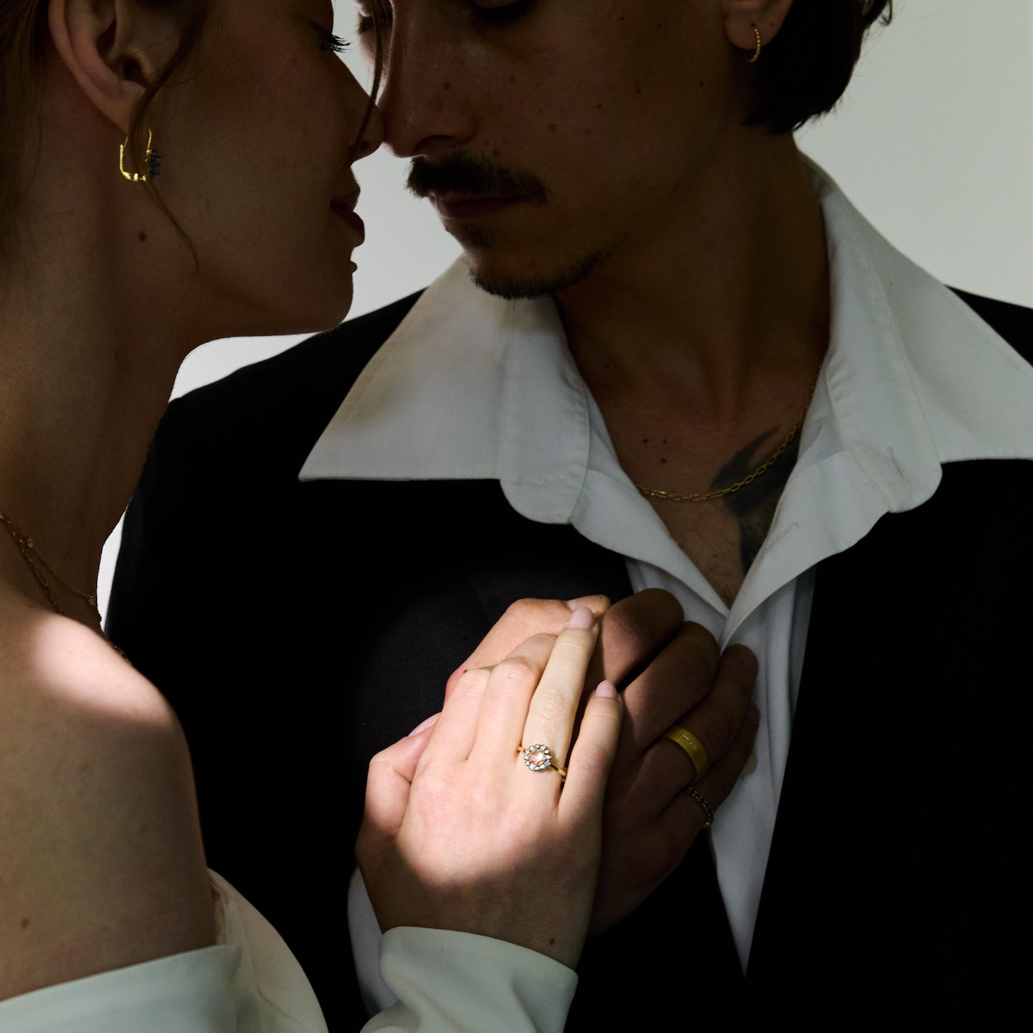 Close-up of a couple holding hands with a focus on their jewelry. Yellow gold ring with a large central rose cut diamond and smaller stones, set in black rhodium plated gold, on the model's hand