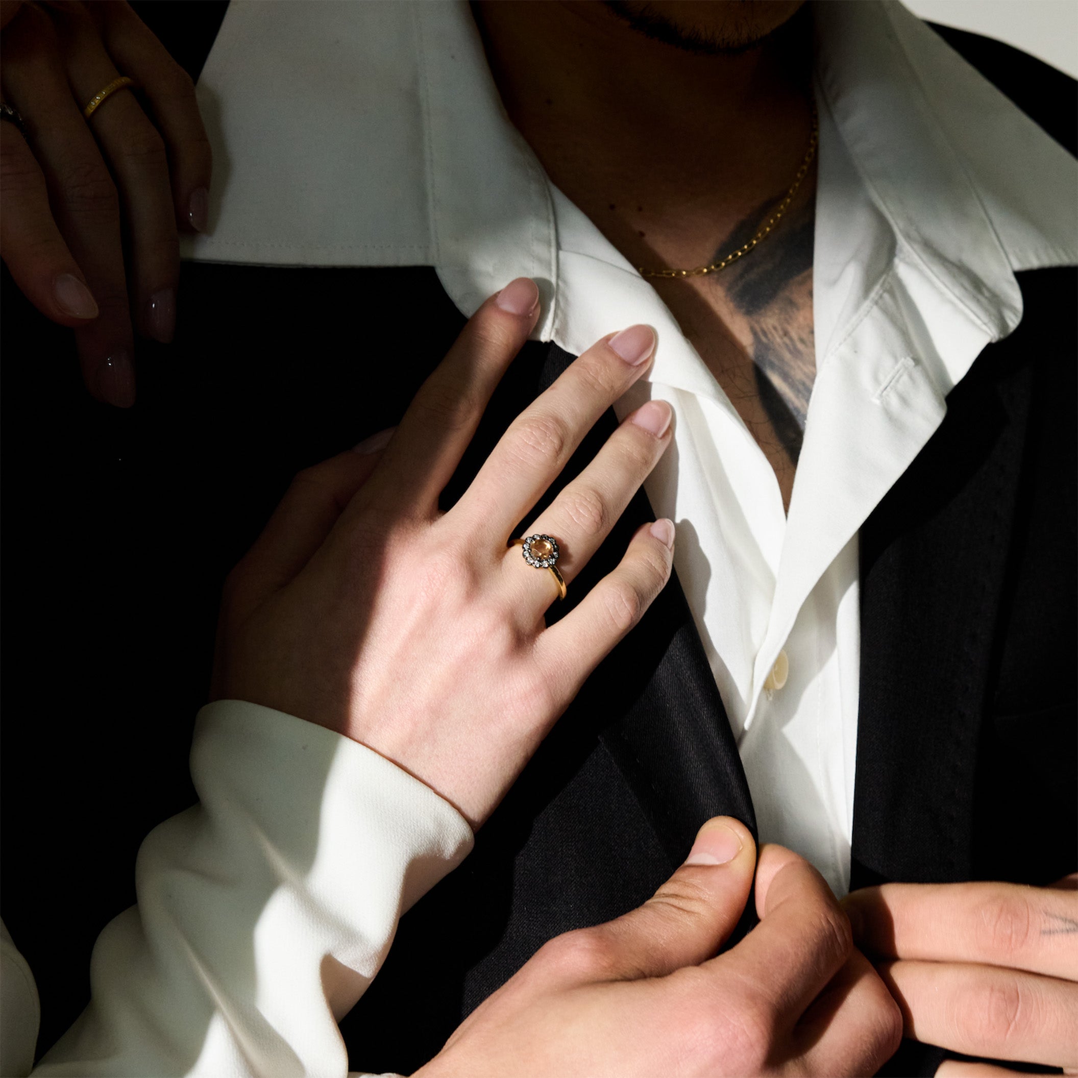 Close-up of a person wearing a rose cut diamond ring, set in black rhodium plated 18k gild, held by another person against a dark background.