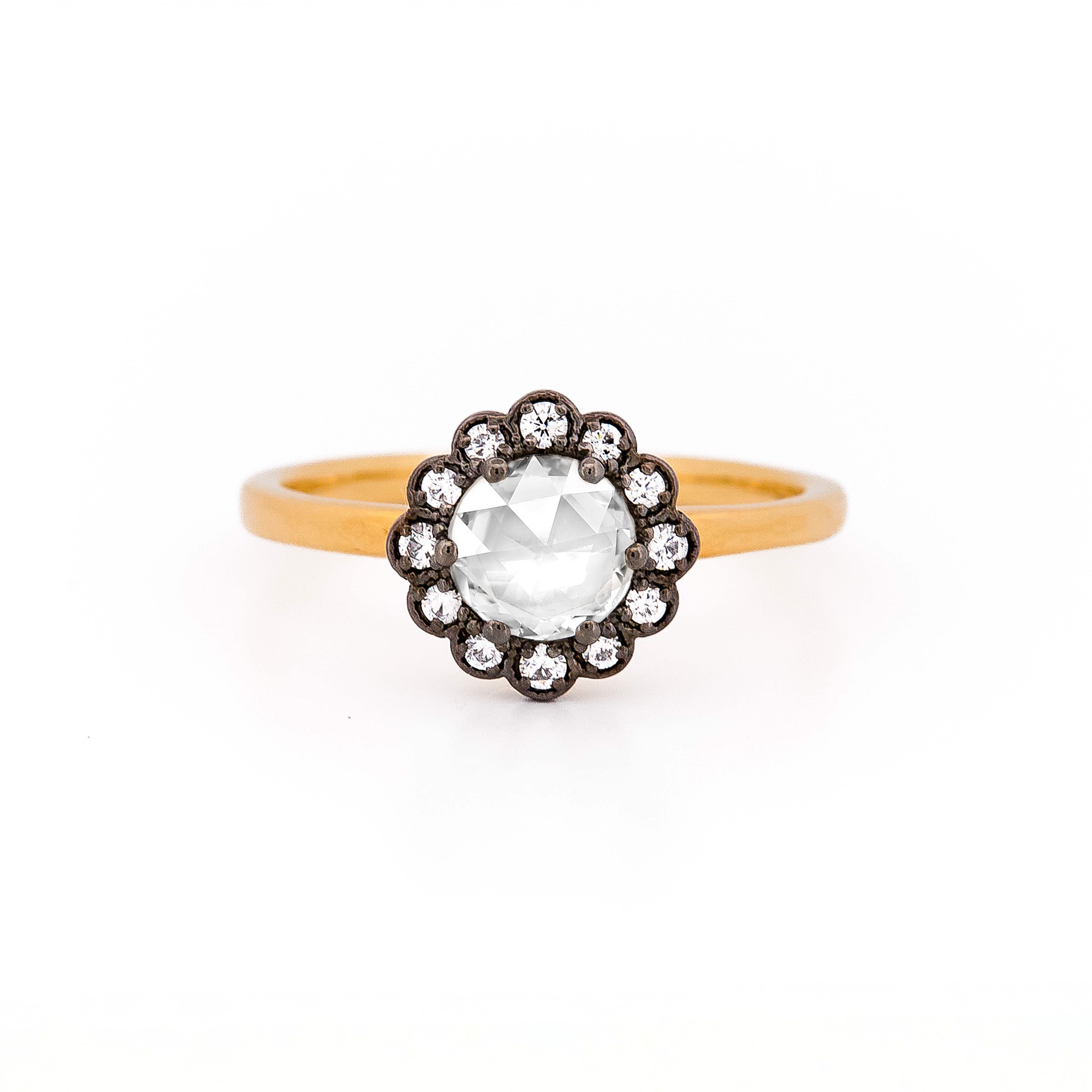 Rose gold ring with a large central rose cut diamond and smaller stones, set in black rhodium plated gold, on a white background