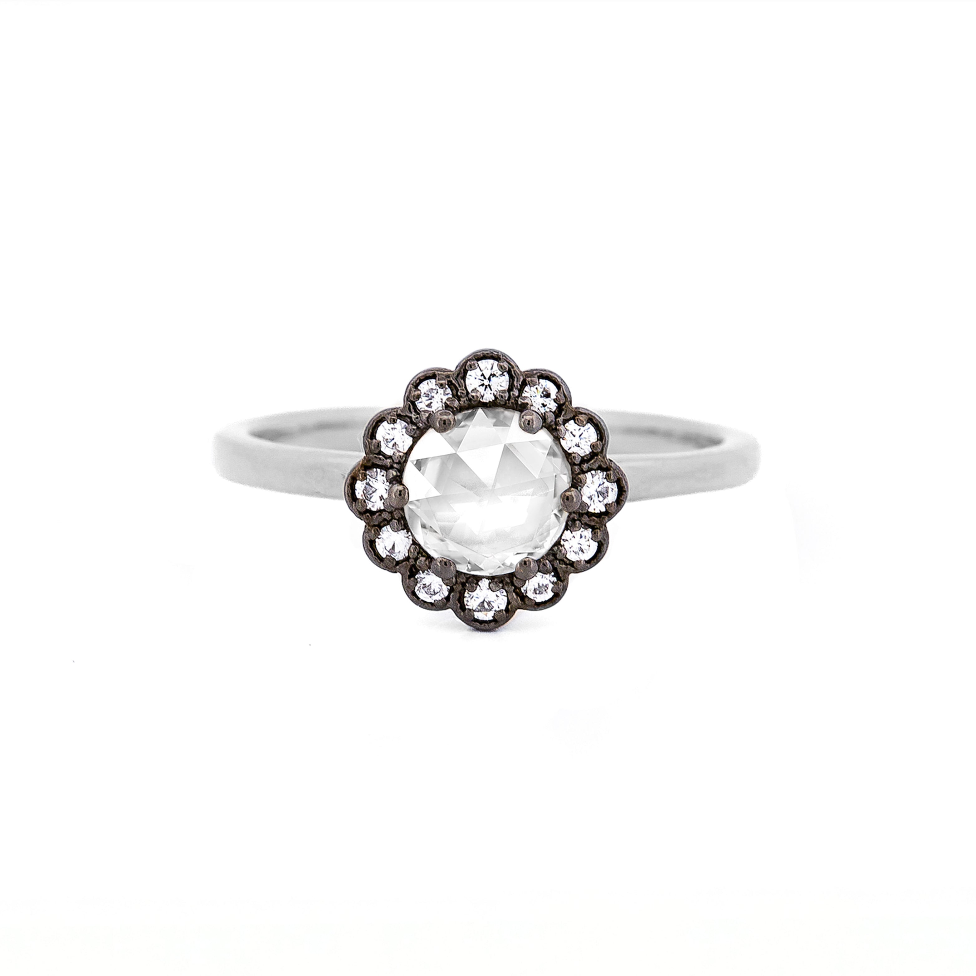 White gold ring with a large central rose cut diamond and smaller stones, set in black rhodium plated gold, on a white background