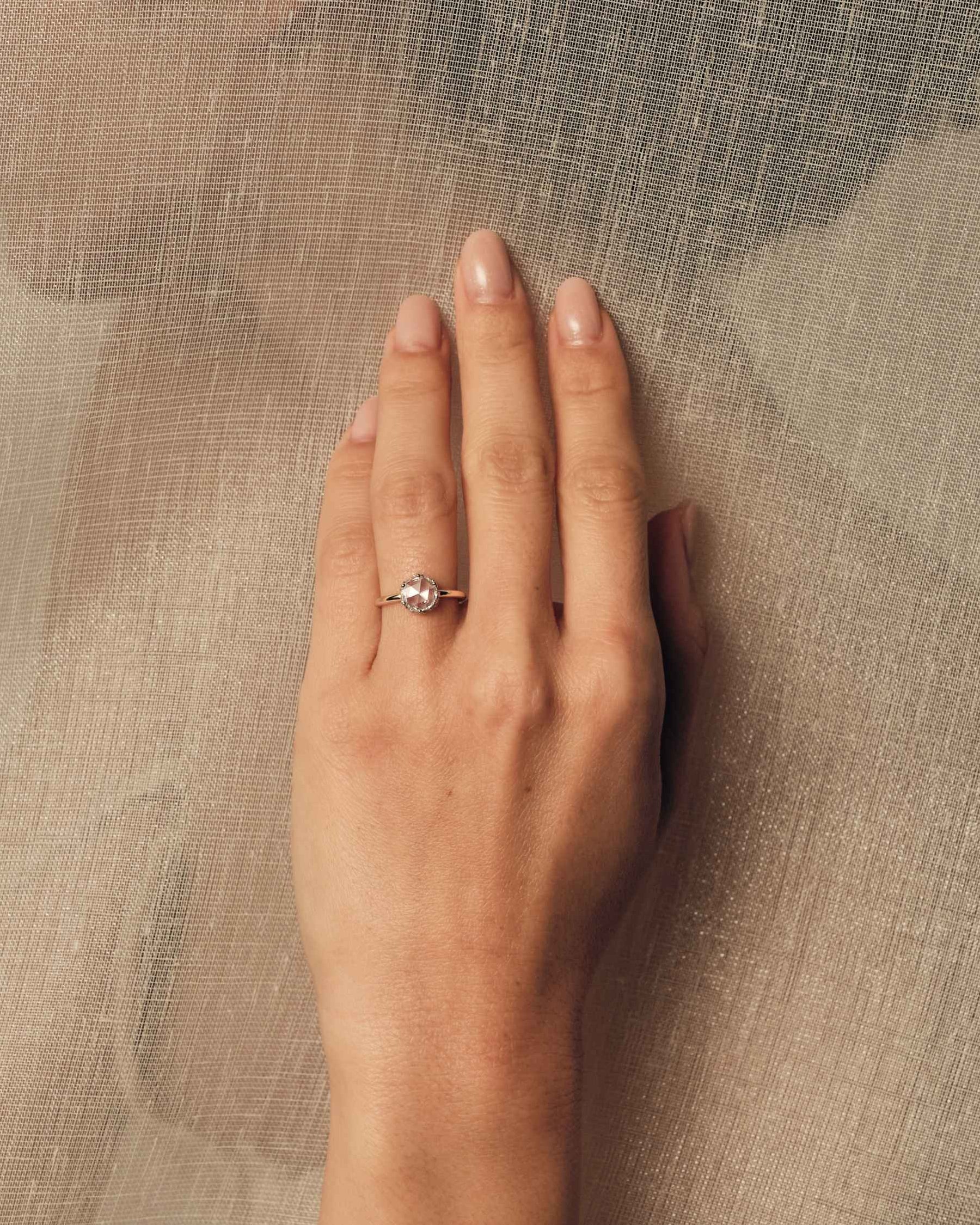 Hand wearing a rose cut diamond ring on a textured beige background.