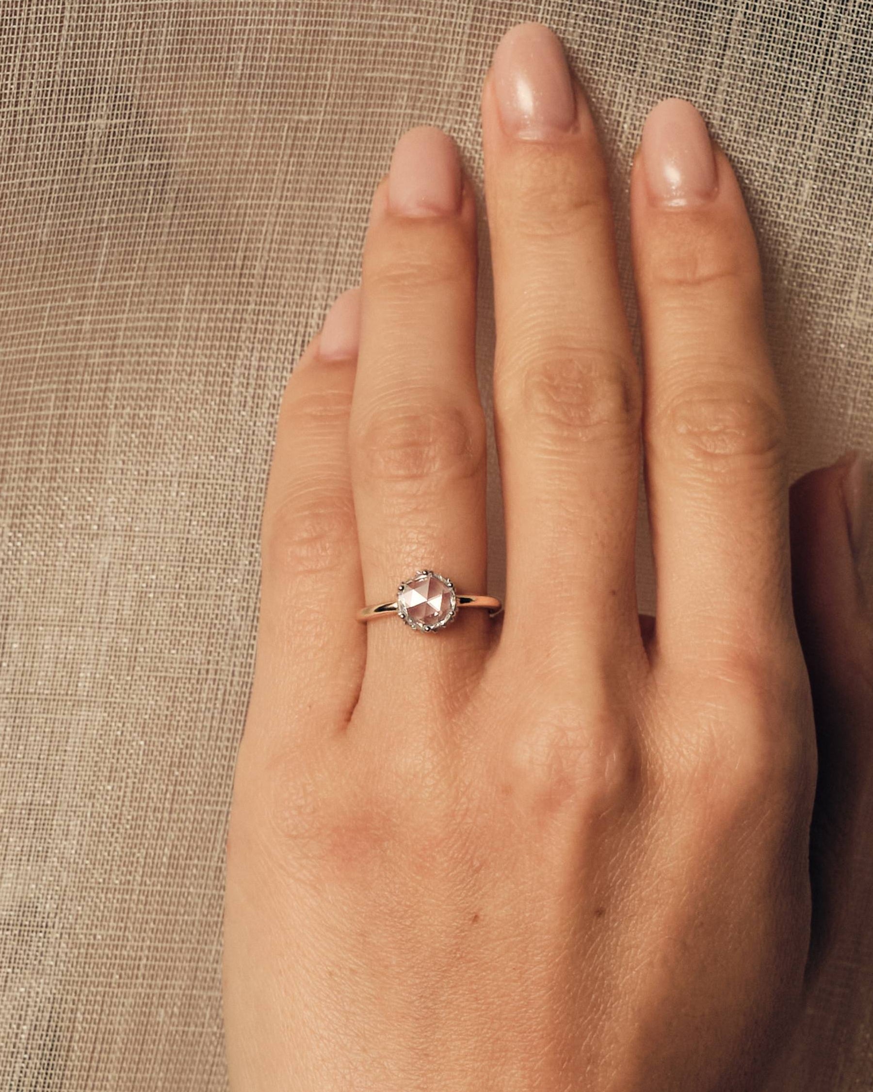 Hand wearing a rose cut diamond ring on a textured beige background.