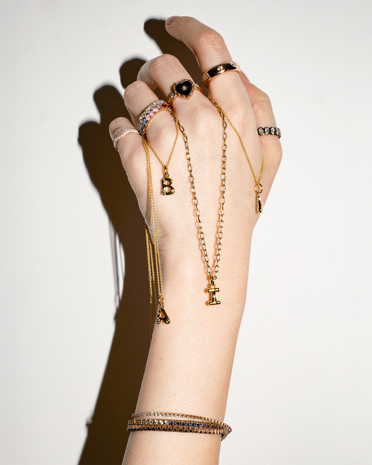 Hand wearing multiple pieces of gold jewelry on a plain background