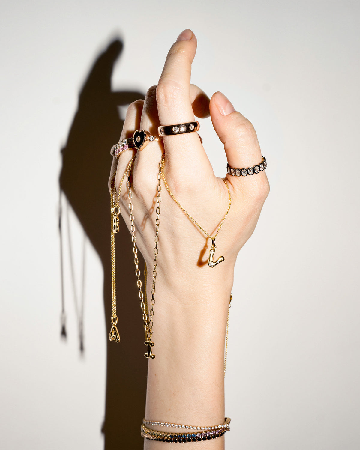 Hand wearing multiple pieces of gold jewelry on a plain background