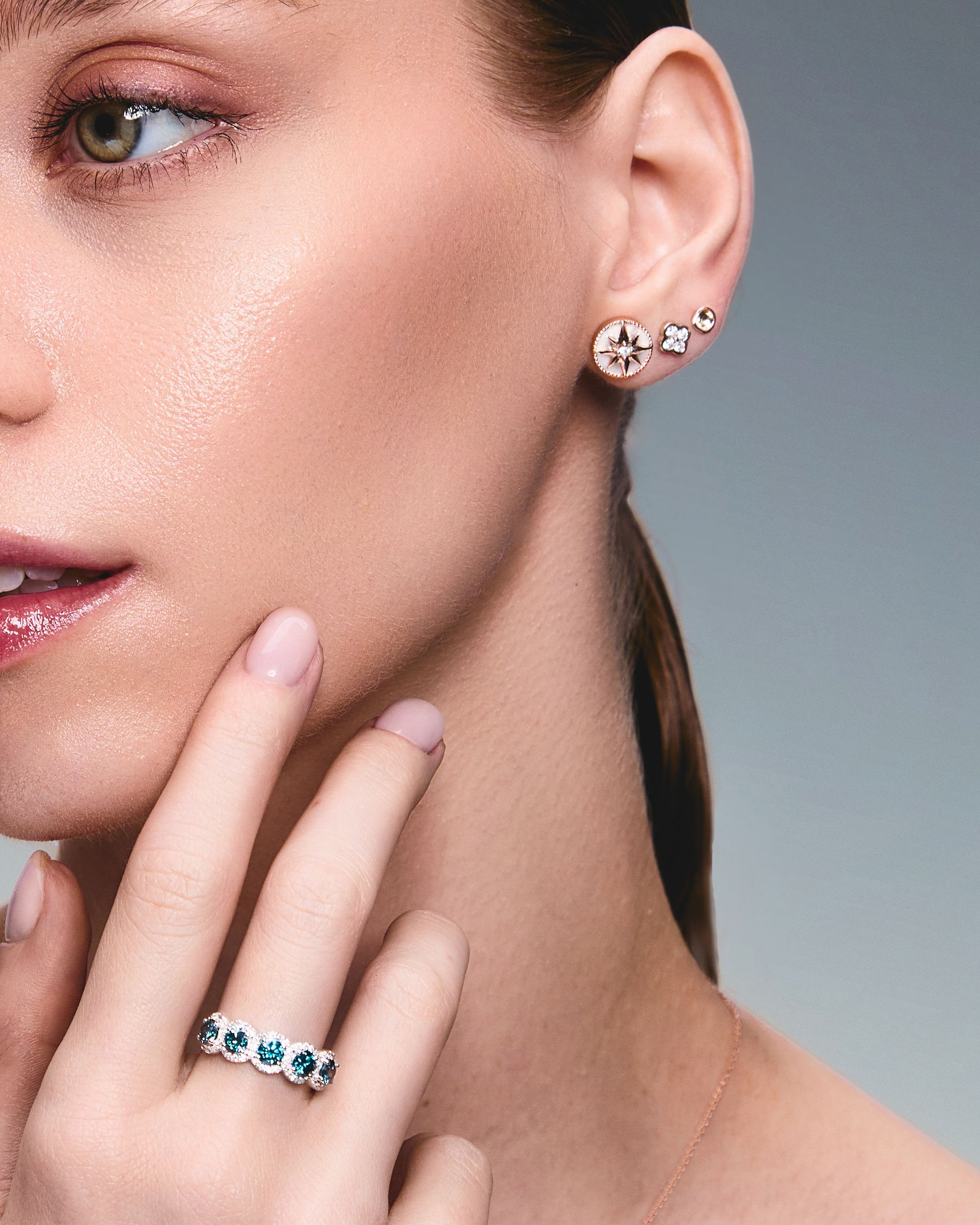 A pair of gold studs earrings with a simple design, resembling a prayer bowl or birds' nest, a clover diamonds earring, a mother of pearl lodestar earring, on an ear.