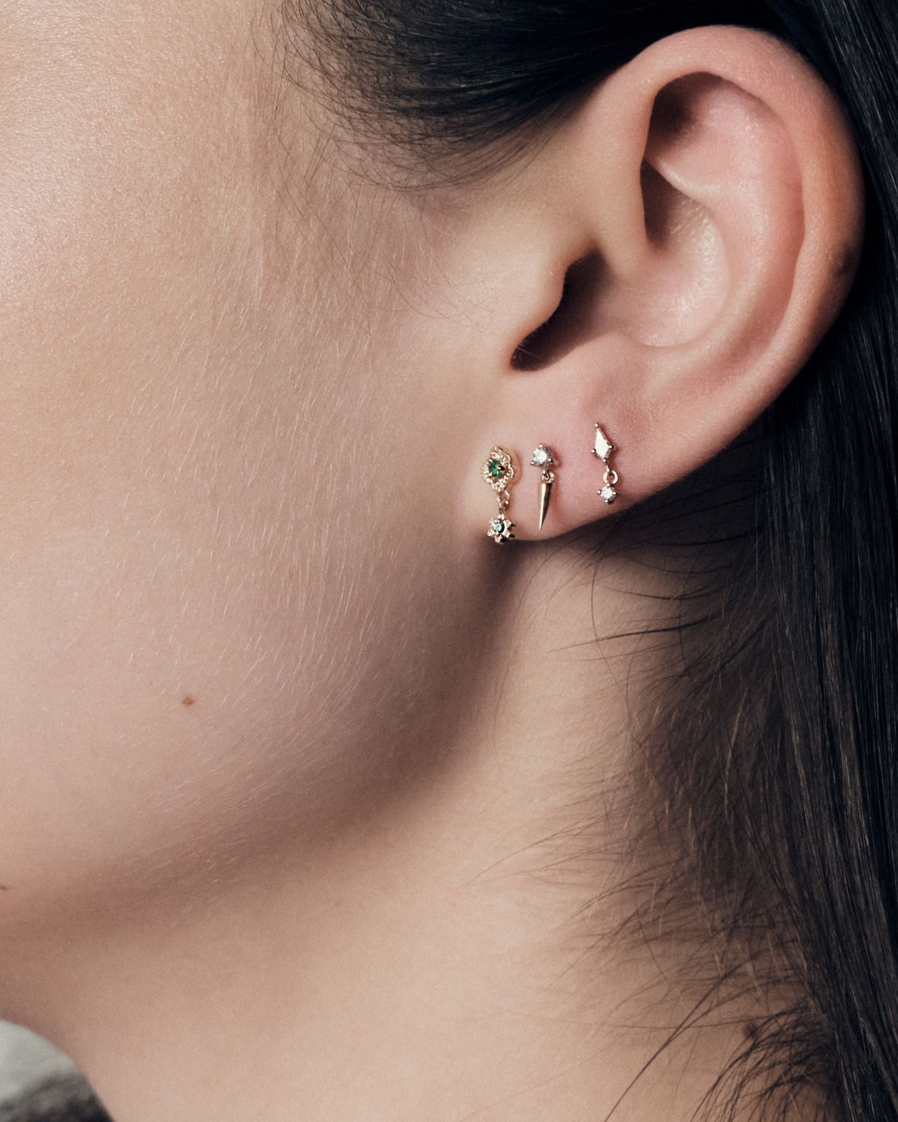 Close-up of an ear wearing a set of earrings, wild rose stud, gold icicle stud and floating kite stud.