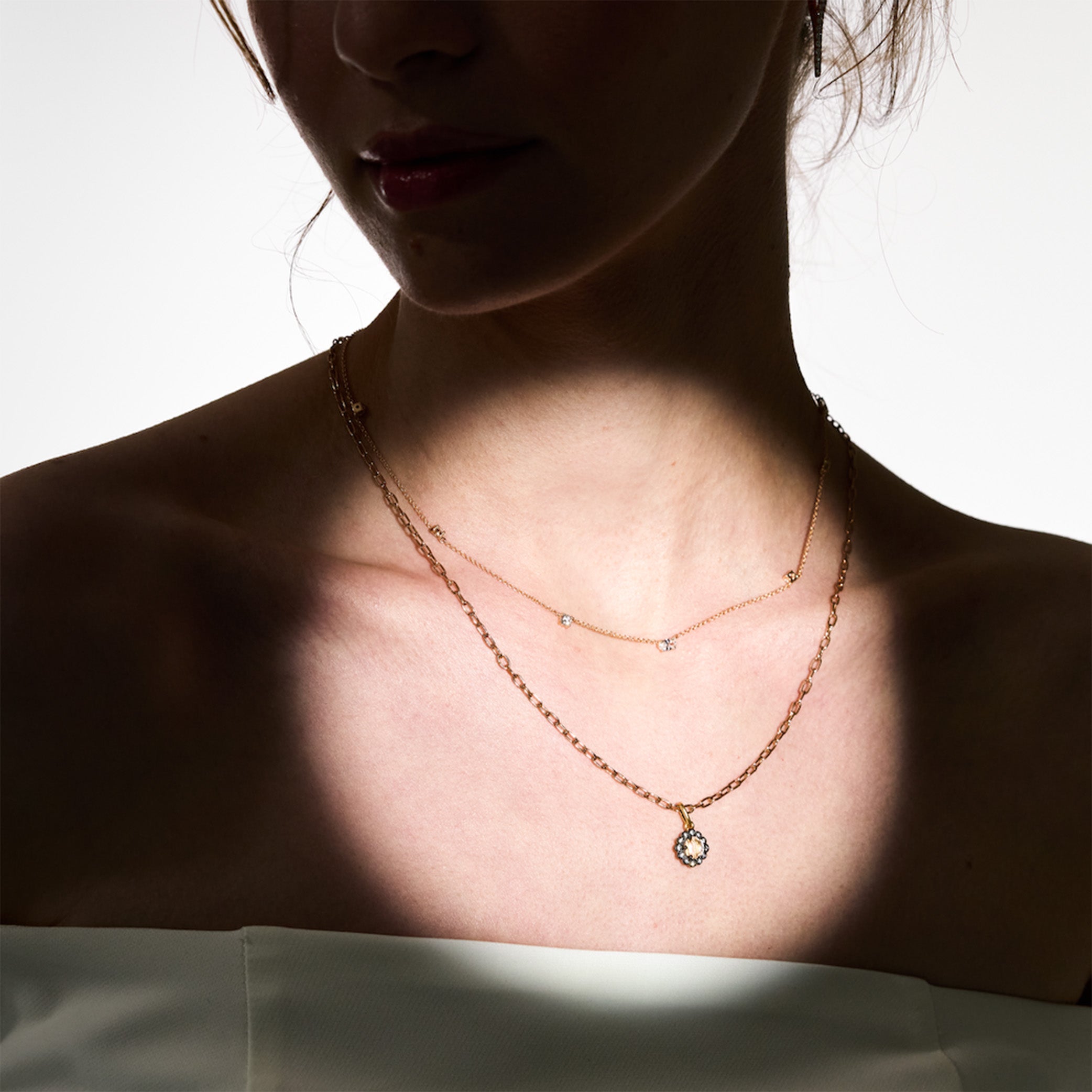 Close-up of a person wearing a delicate necklace with a small pendant on a plain background