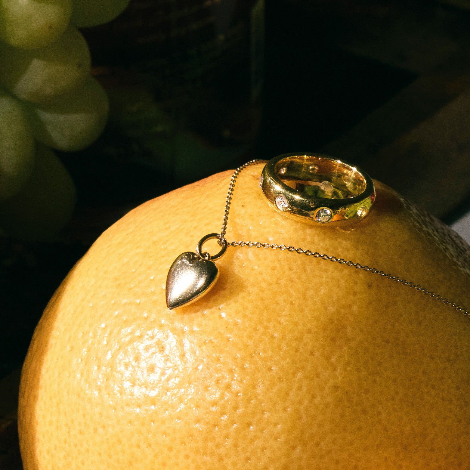 Necklace with a heart pendant and a gold band ring with diamonds on a grapefruit