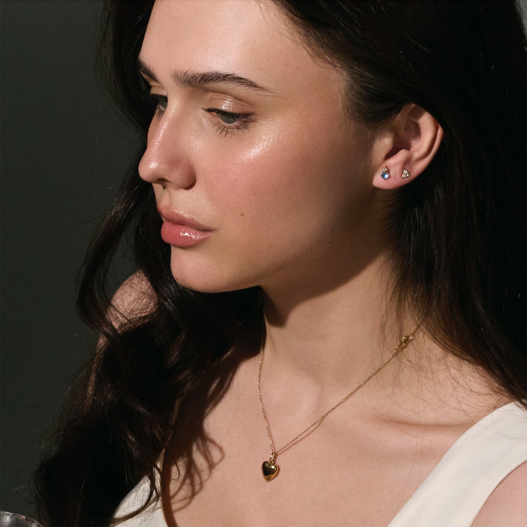 Woman wearing a gold necklace with a heart pendant against a dark background