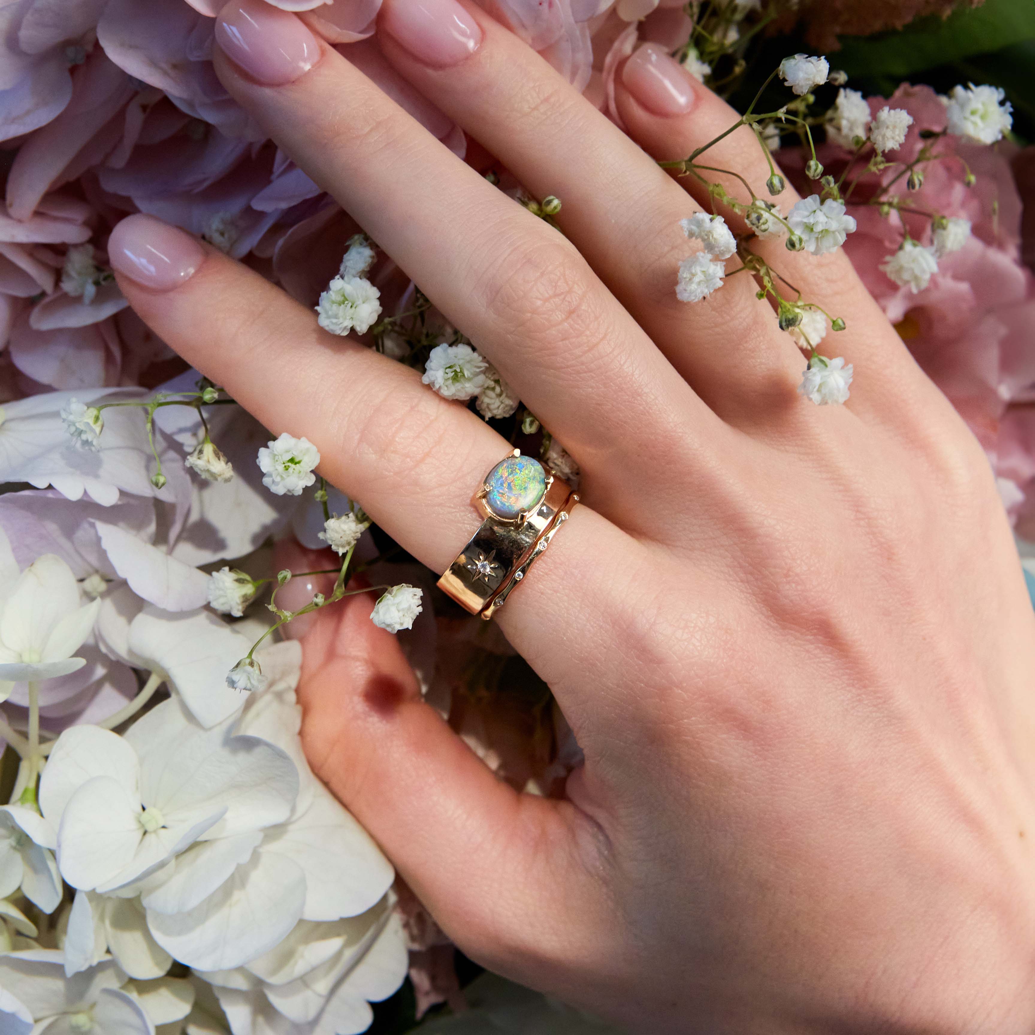 australian opal band ring in rose gold on hand surrounded by beautiful flowers