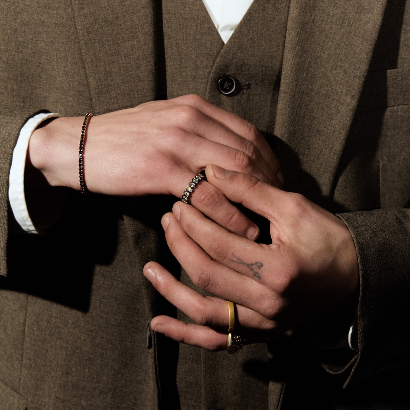Close-up of two hands with rings, one wearing a brown suit.