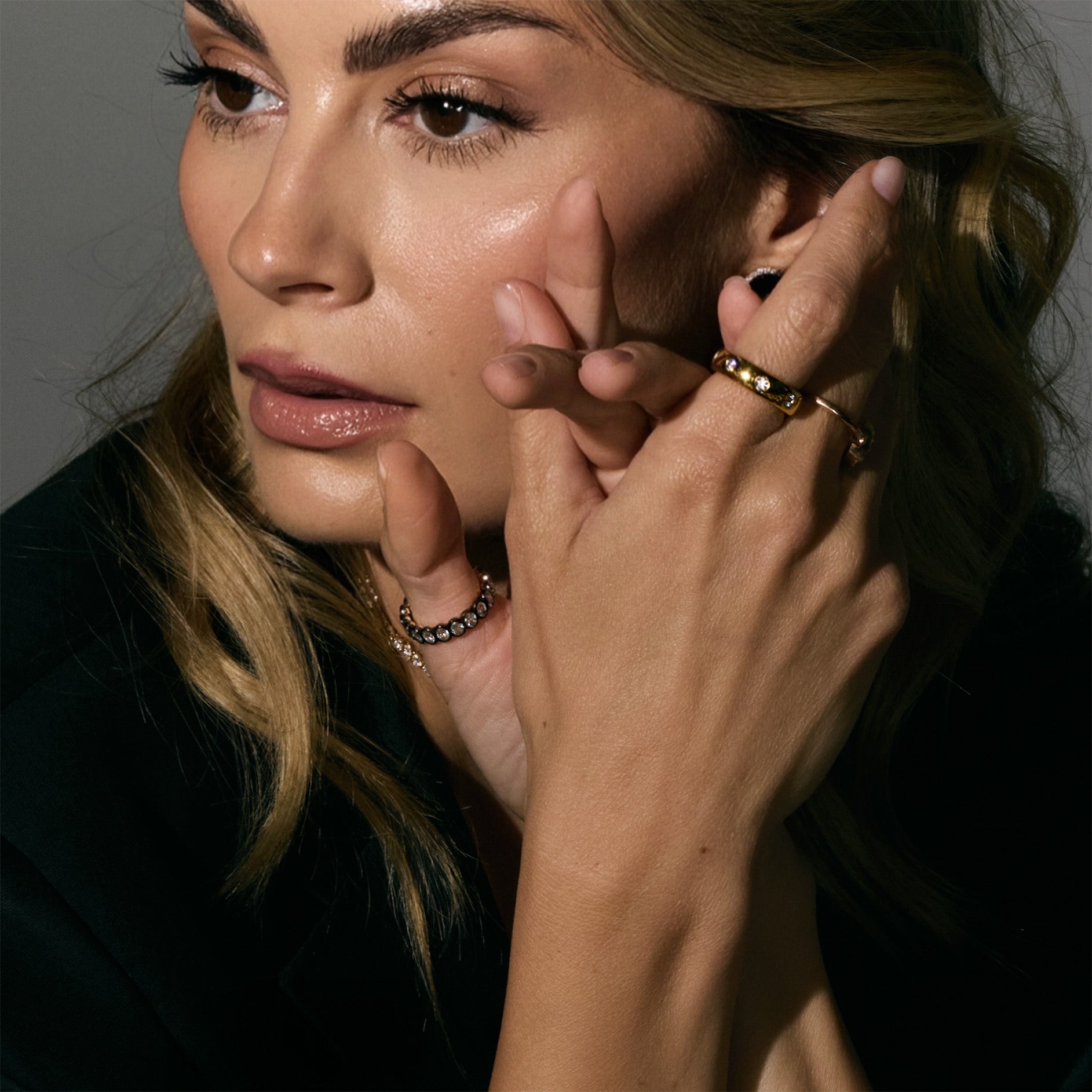 Close-up of a woman with her hand near her face, wearing multiple rings.
