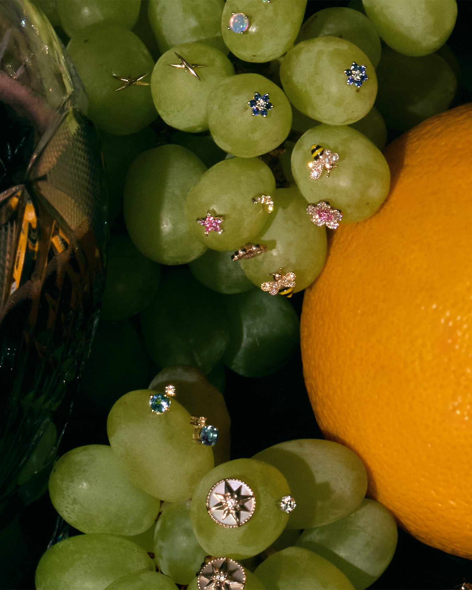 Close-up of green grapes with diamonds and precious gemstones earrings and an orange on a dark background