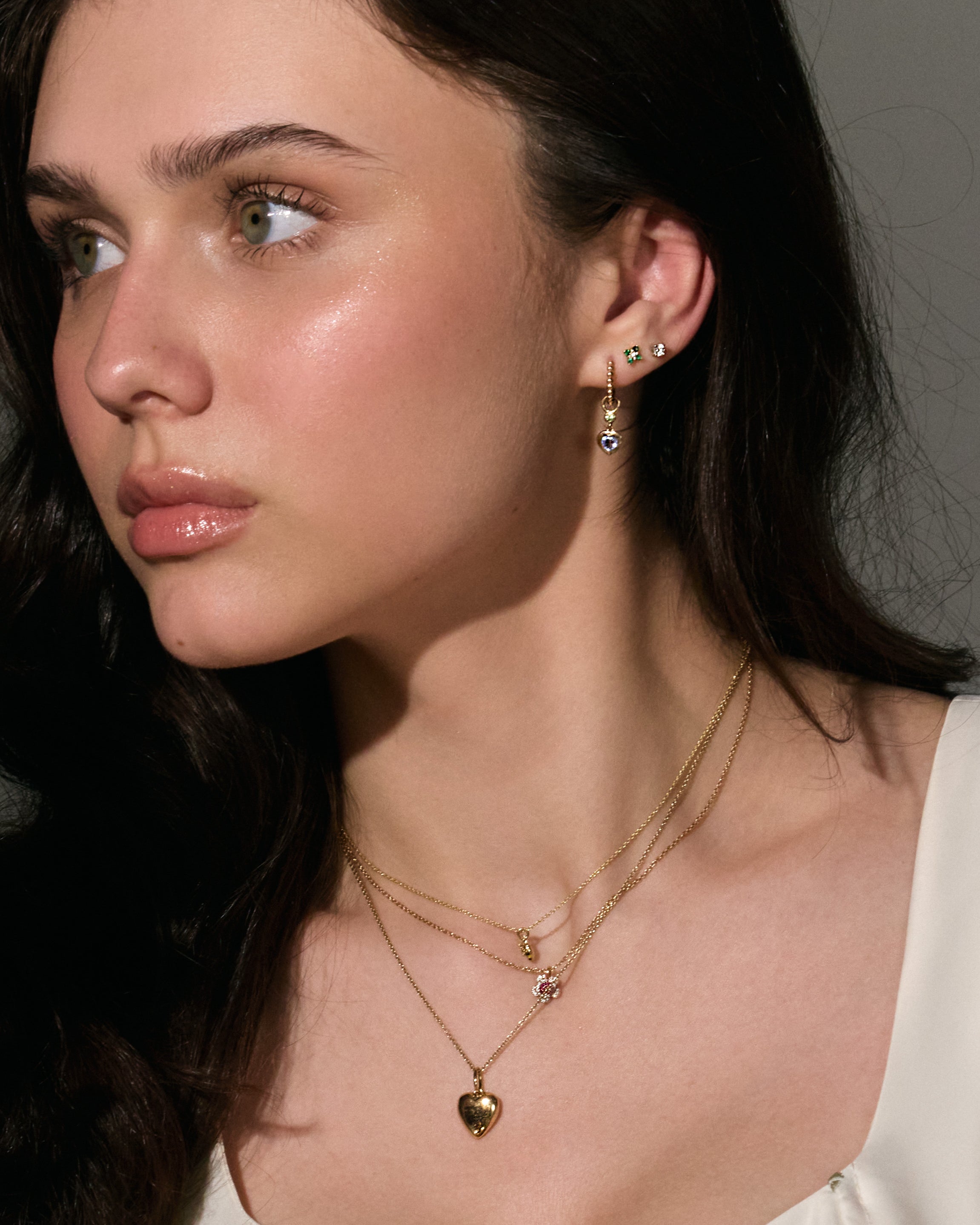 Woman wearing gold necklaces and earrings against a neutral background