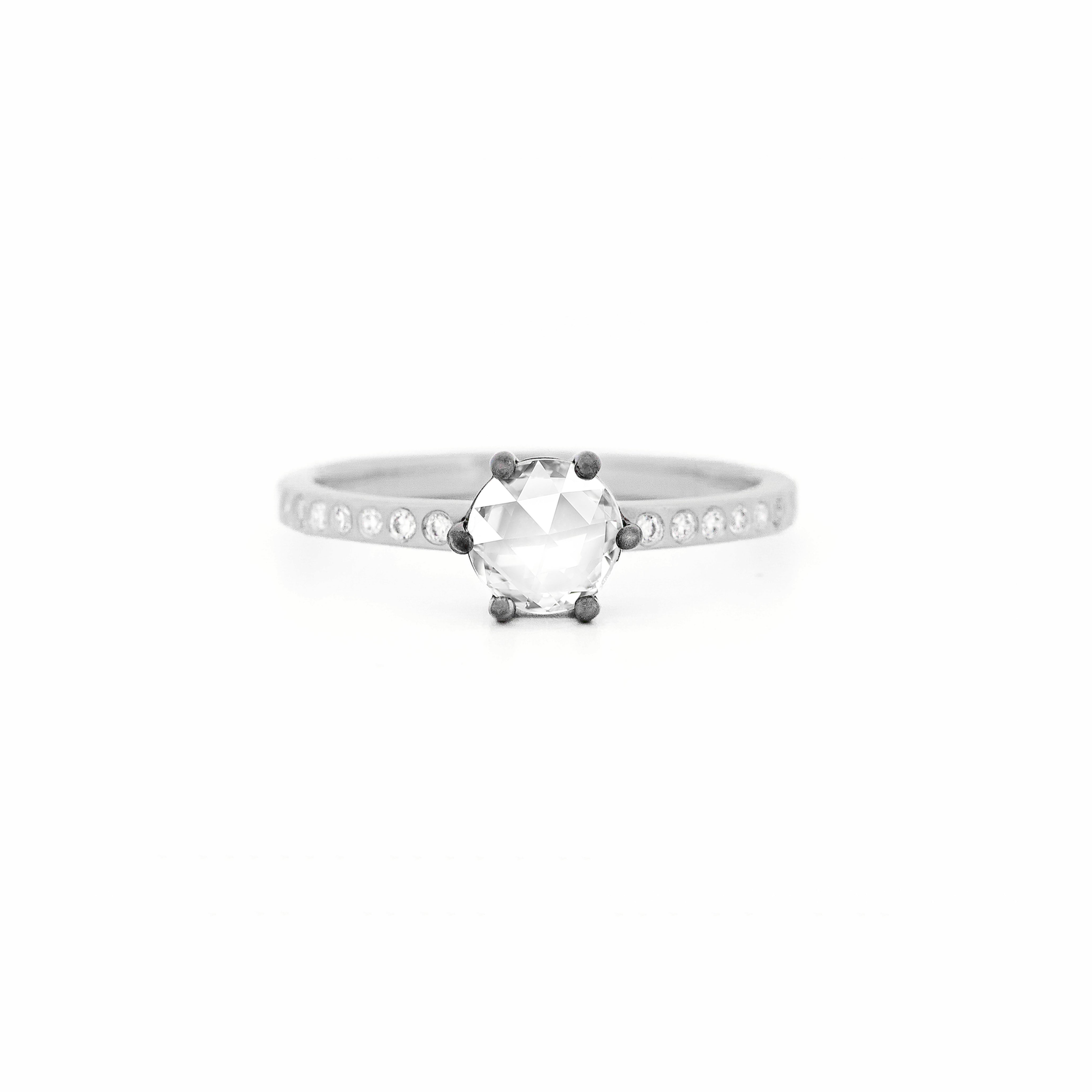 Ring with a large central rose-cut diamond and smaller side diamonds on a white gold band against a white background