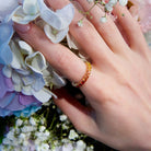 Beautiful eternity rainbow sapphires ring on hand. The hand is resting on a wild colourful flowers. 