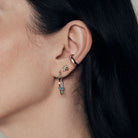 Close-up of a person wearing gold hoop earrings with diamonds and australian opals, baby bee enamela and diamond studs and marquise diamond earcuff.
