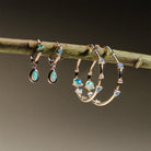 Gold hoop earrings with embedded australian opals and diamonds on a branch.