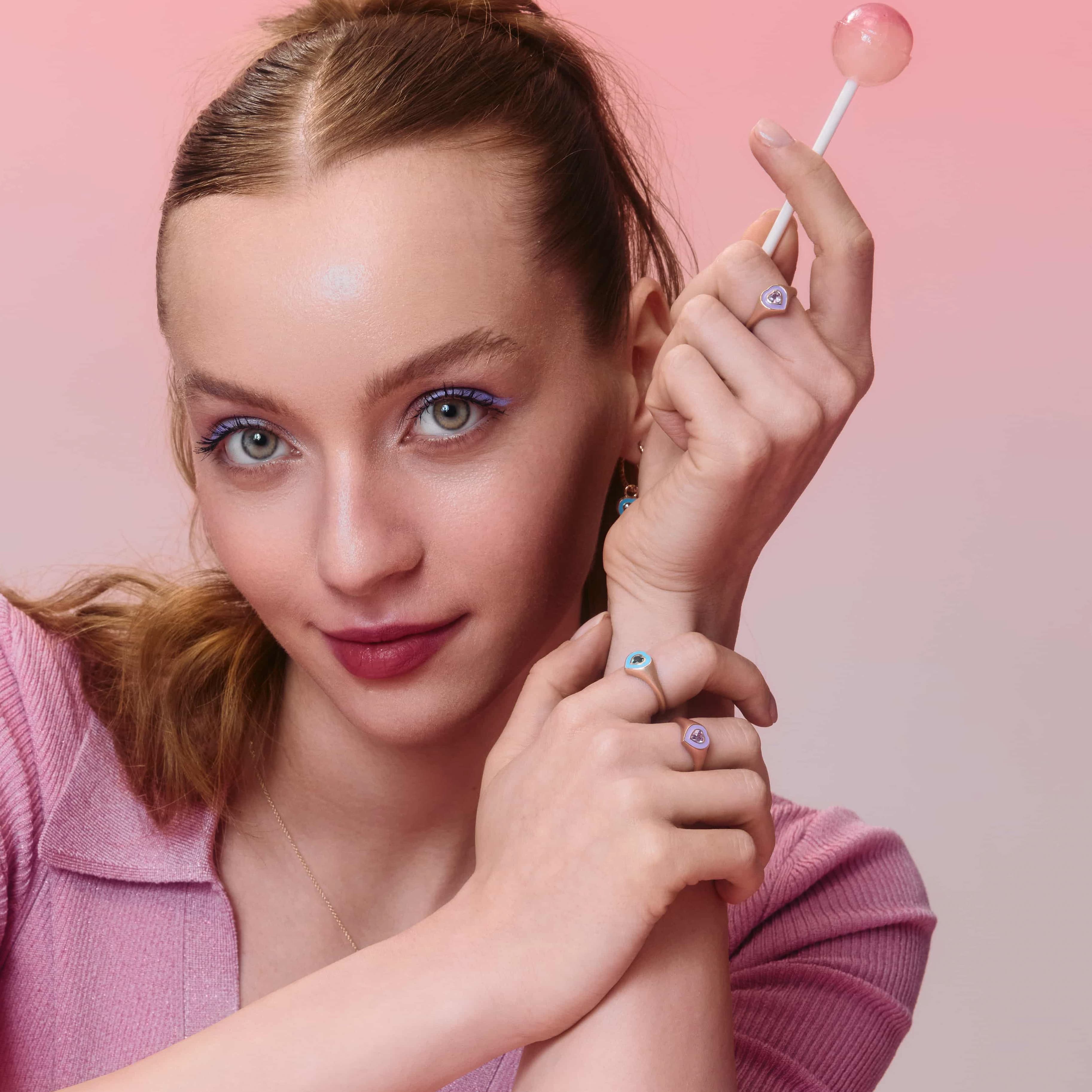 A girl holding a lollipop in her hand and wearing three colorful enamel rings with sapphire accents.