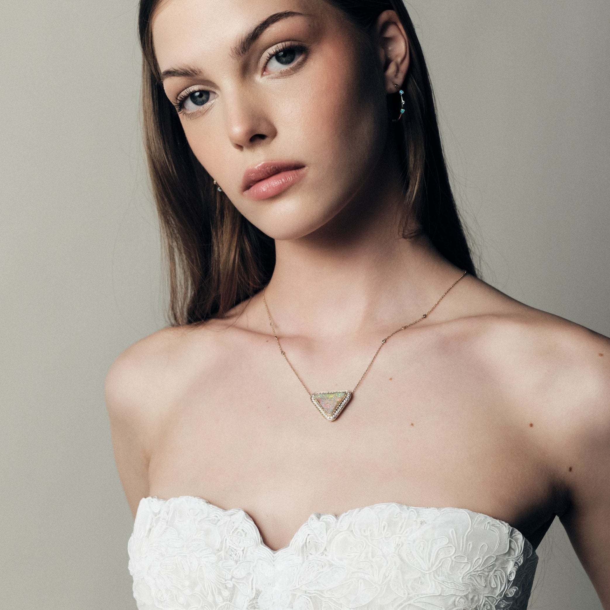 Woman wearing a white strapless dress and a gold necklace with diamonds and a trillion Australian Opal Boulder pendant against a plain background