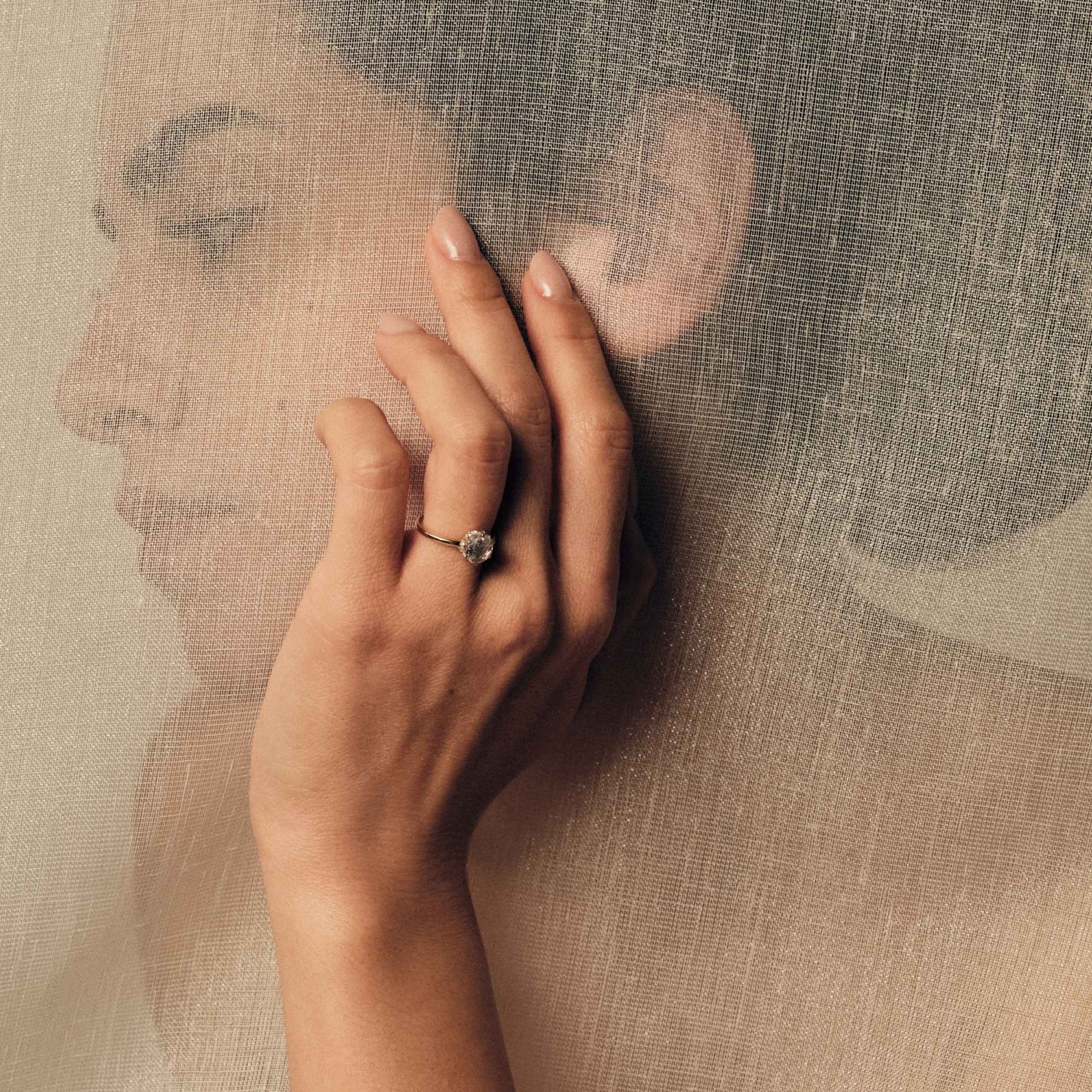 Hand wearing a rose cut diamond ring on a textured beige background.