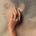 Hand wearing a rose cut diamond ring on a textured beige background.
