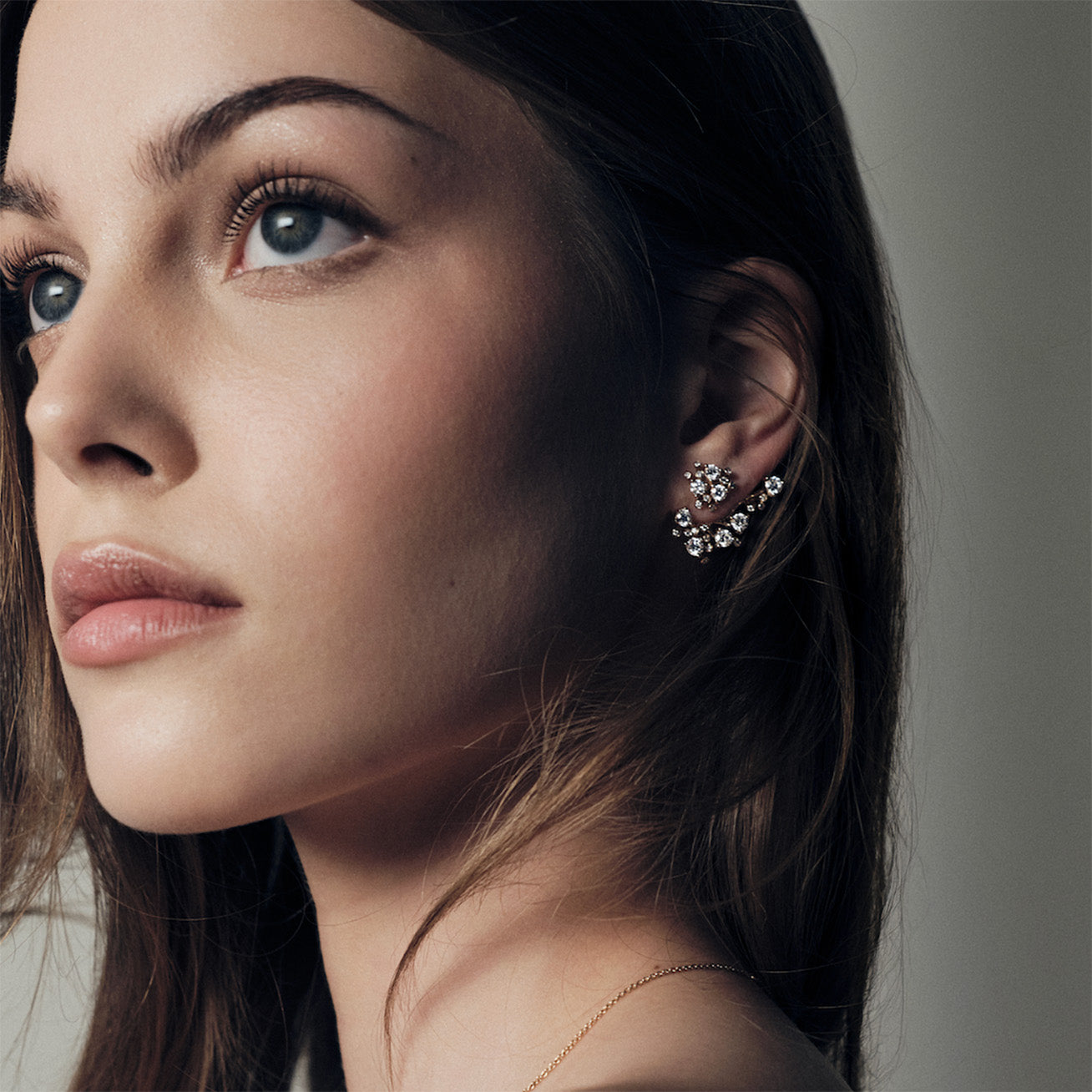 Close-up of a woman wearing a delicate bloom gold and diamonds earring with a neutral background