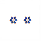 Pair of floral earrings with blue sapphires and diamonds and gold accents on a white background