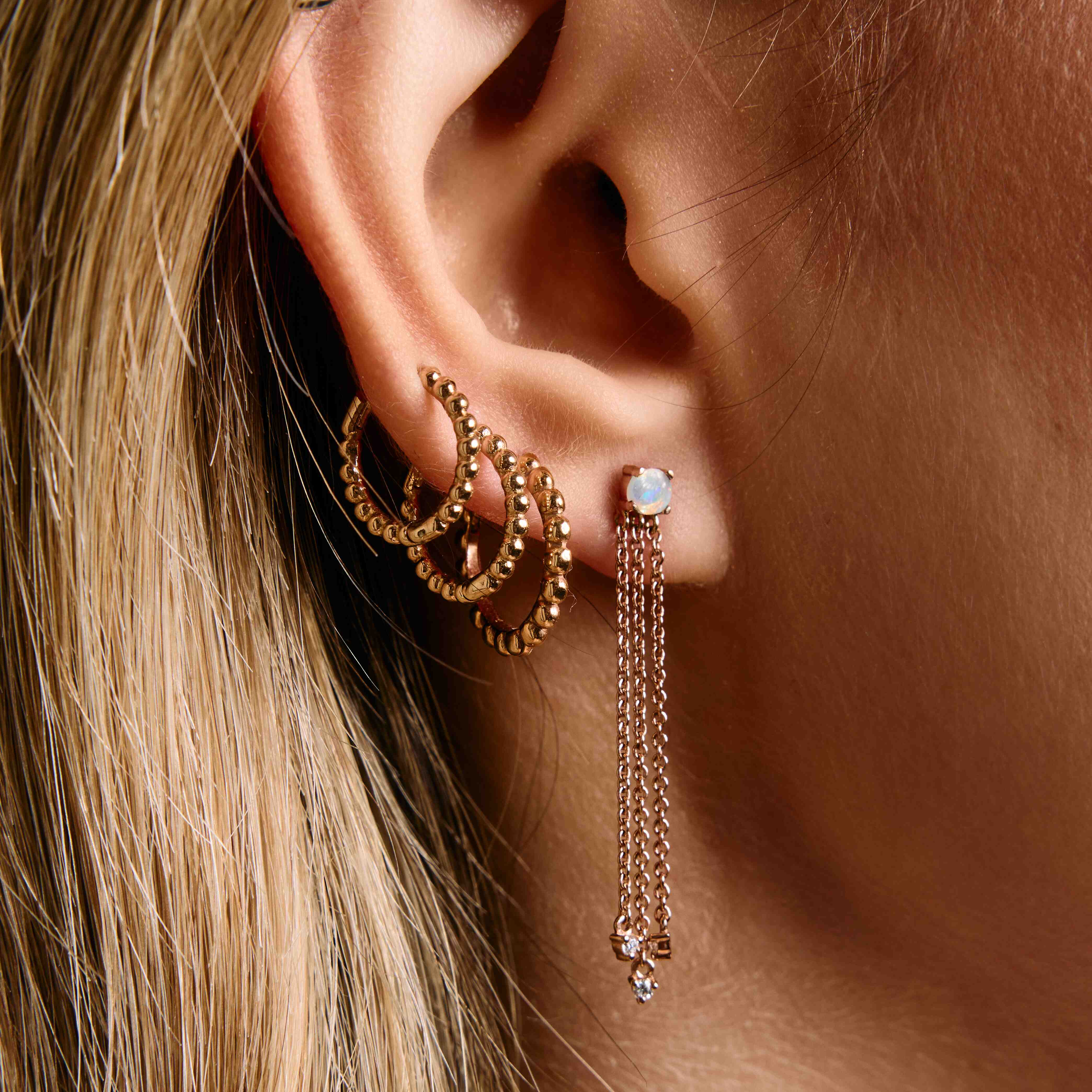A pair of gold hoop earrings with a beaded design, mix and match on ear