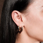 Close-up of an ear wearing multiple hoop earrings, thick gold hoops, floating marquise diamond stud, simple beaded hoop, with a blurred background