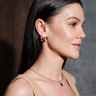 Woman wearing multiple hoop earrings, thick gold hoops, floating marquise diamond stud, simple beaded hoop, with a dark background